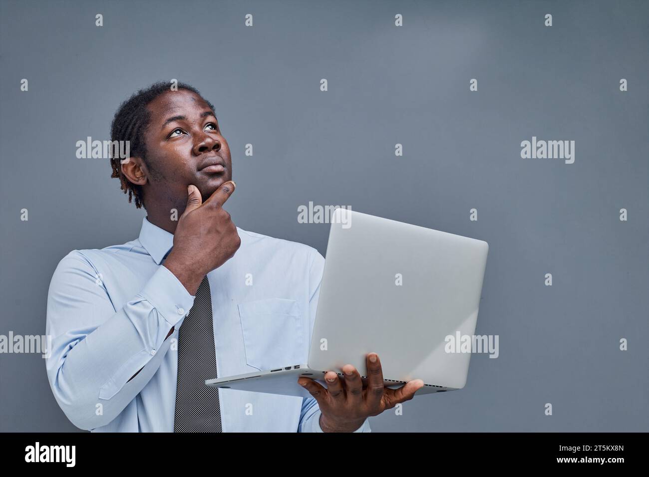 Junger afroamerikaner auf grauem Hintergrund, der einen Laptop hält. Zeigt Daumen nach oben Stockfoto
