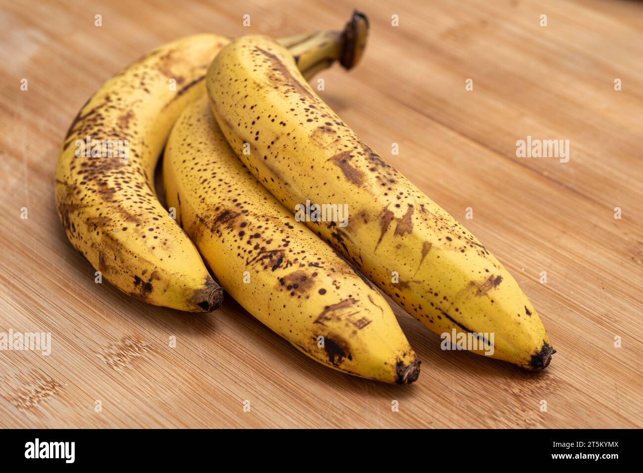 Drei reife Bananen auf einem hölzernen Schneidebrett. Stockfoto