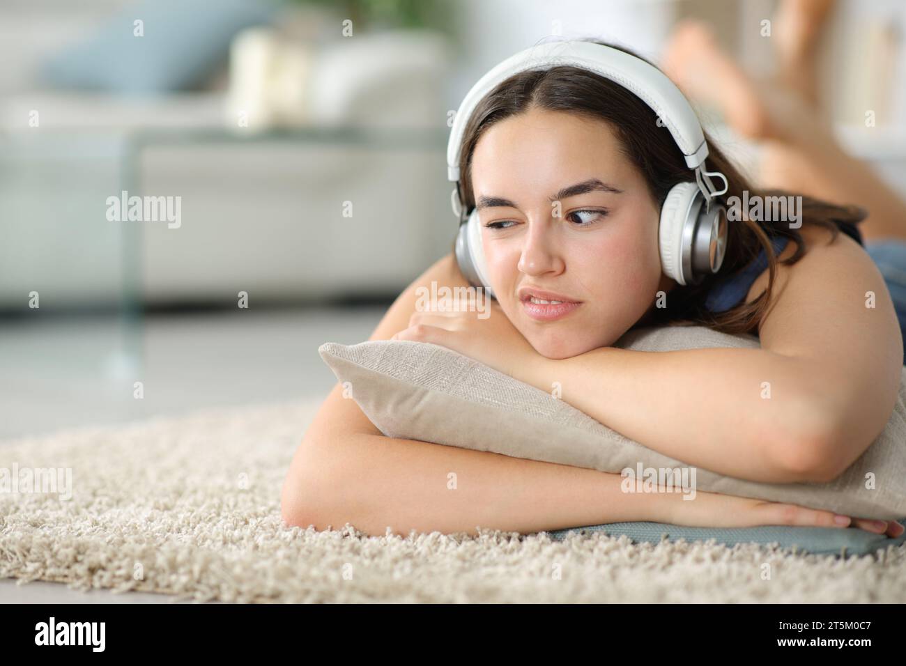 Enttäuschte Frau, die Musik hört, mit Kopfhörern, die zu Hause auf einem Teppich liegen Stockfoto
