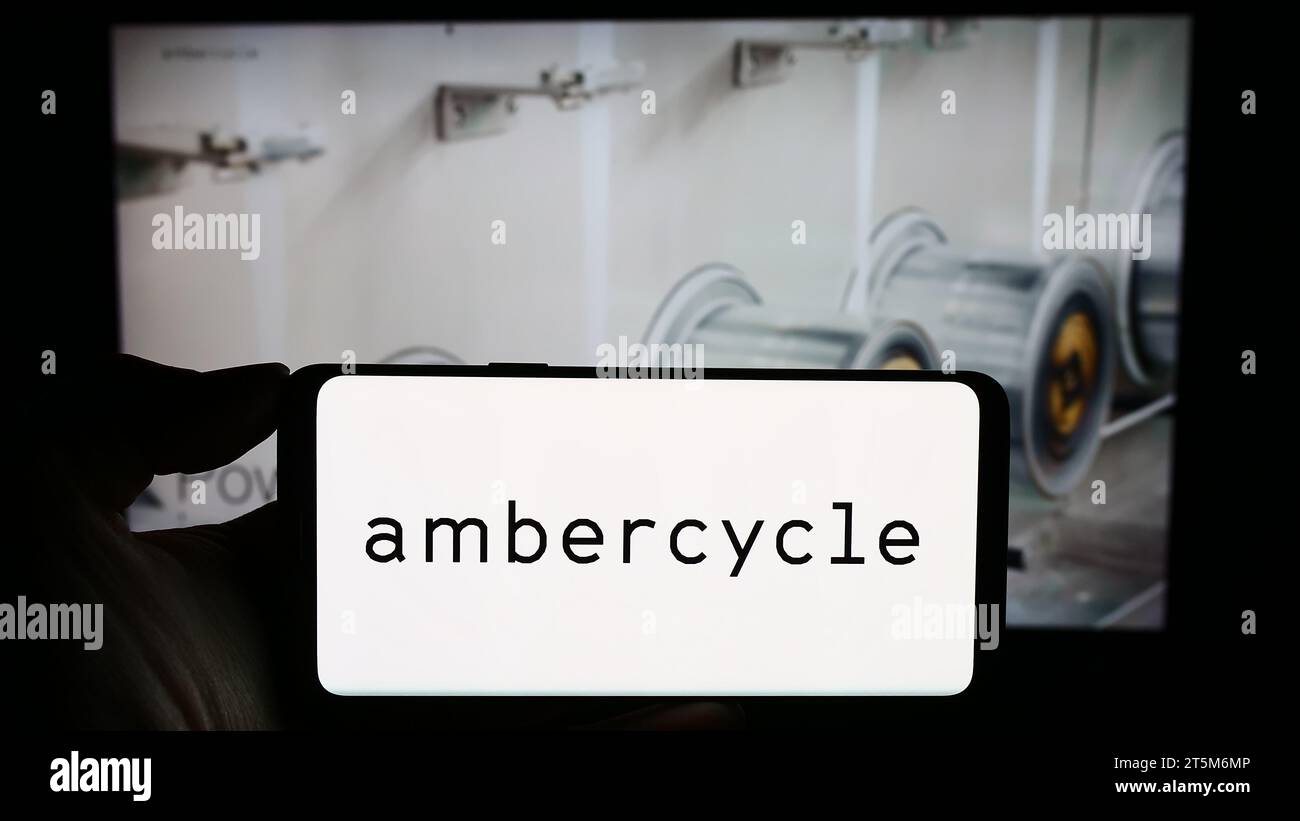 Person, die ein Mobiltelefon mit dem Logo des US-amerikanischen Materialforschungsunternehmens Ambercycle Inc. Vor der Unternehmenswebseite hält. Schwerpunkt auf dem Display des Telefons. Stockfoto