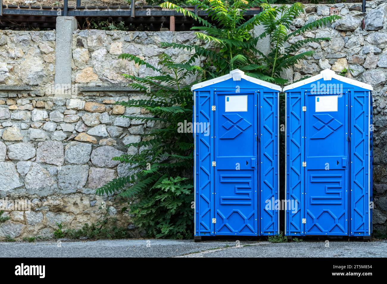 Öffentliche tragbare Bio-WC-Kabinen an einer Steinmauer an der Stadtstraße. Mobile Toiletten für Gäste im Stadtpark installiert. Blaue Sanitäreinrichtungen in der Stadt Stockfoto