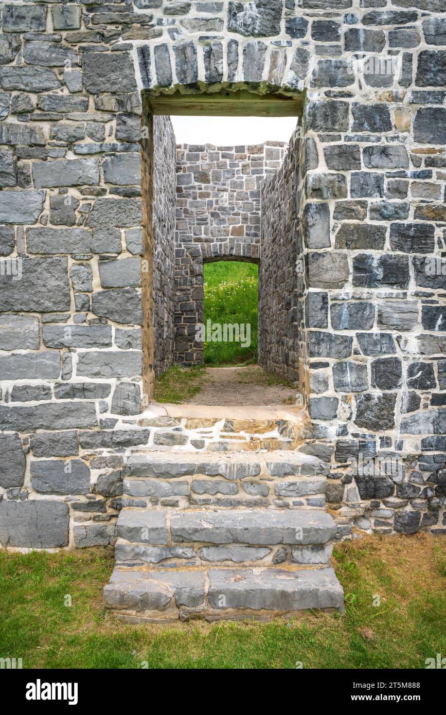 Blick nach oben zu drei abgenutzten Stufen, die einen steinernen Türrahmen umgeben, der einen inneren Durchgang und grünes Gras am Crown Point State Historic Site in New York einrahmt. Stockfoto