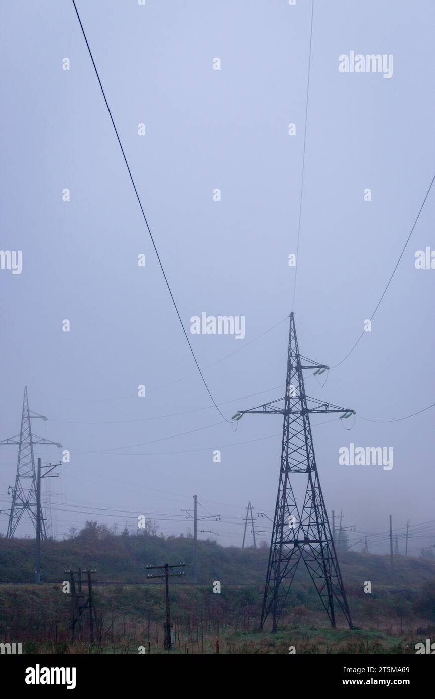 Stromleitungen am nebeligen Morgen im Herbstfeld. Elektroindustriekonzept. Elektrische Geräte in der Natur. Hochspannungskonzept. Stromleitungen. Stockfoto