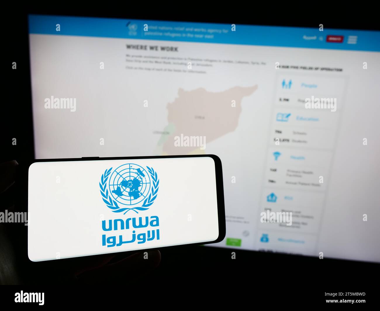 Person, die ein Handy mit dem Logo des United Nations Plalestine Flüchtlingshilfswerks UNRWA vor der Webseite hält. Schwerpunkt auf dem Display des Telefons. Stockfoto