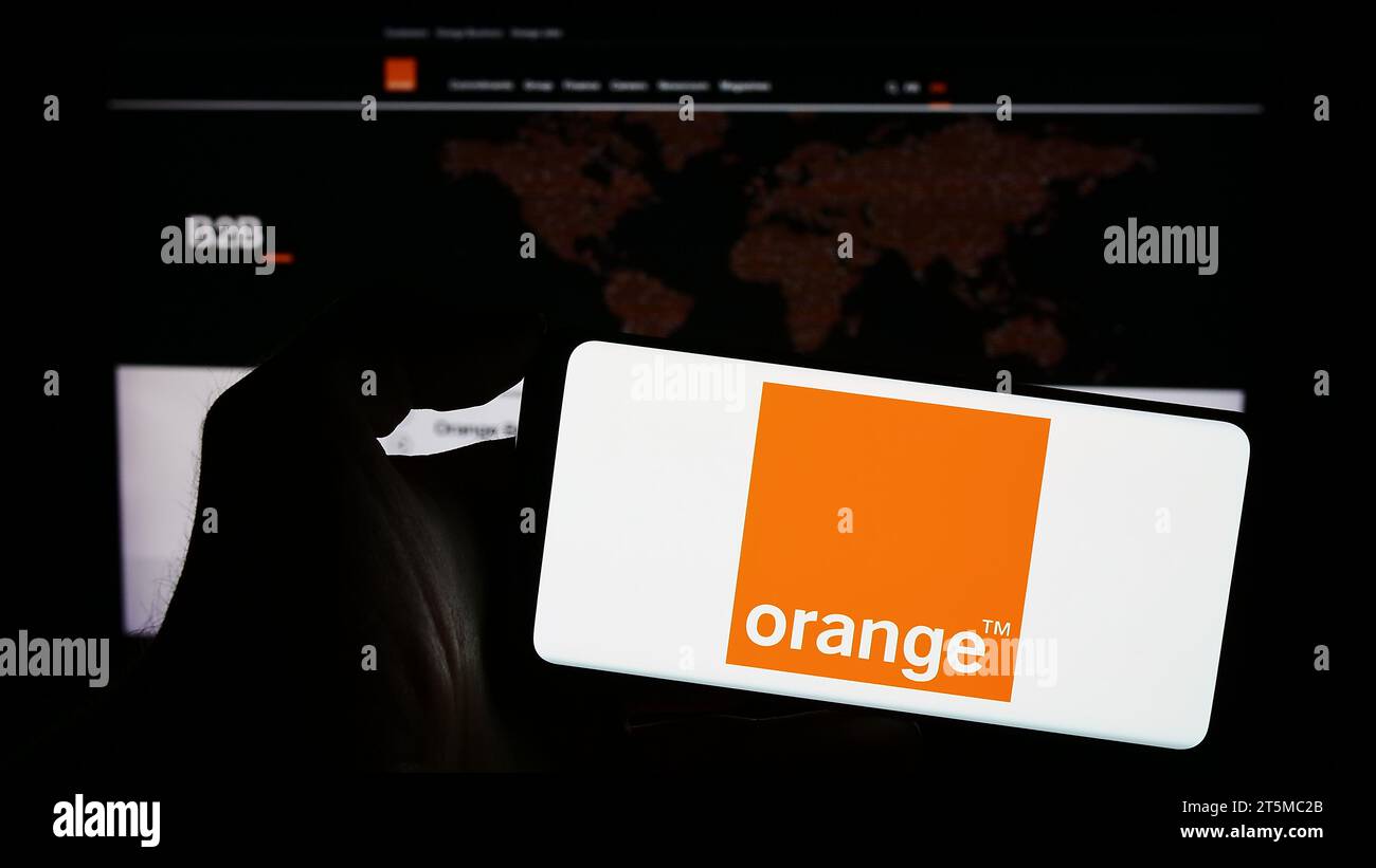 Person, die ein Mobiltelefon mit dem Logo des französischen Telekommunikationsunternehmens Orange S.A. vor der Website des Unternehmens hält. Schwerpunkt auf dem Display des Telefons. Stockfoto