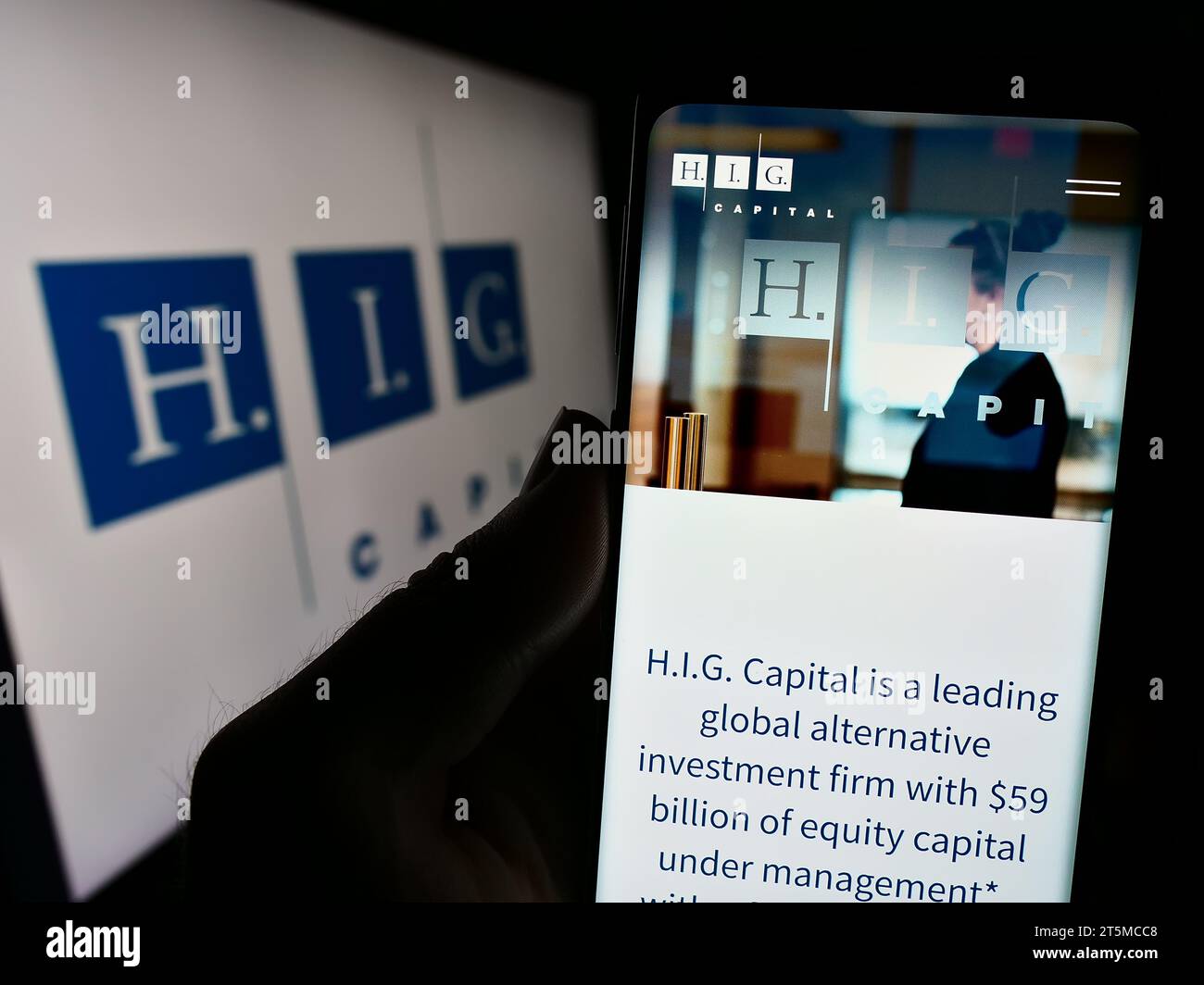 Person mit Mobiltelefon und Website der US-Investmentgesellschaft H.I.G. Capital LLC vor dem Firmenlogo. Konzentrieren Sie sich auf die Mitte des Telefondisplays. Stockfoto