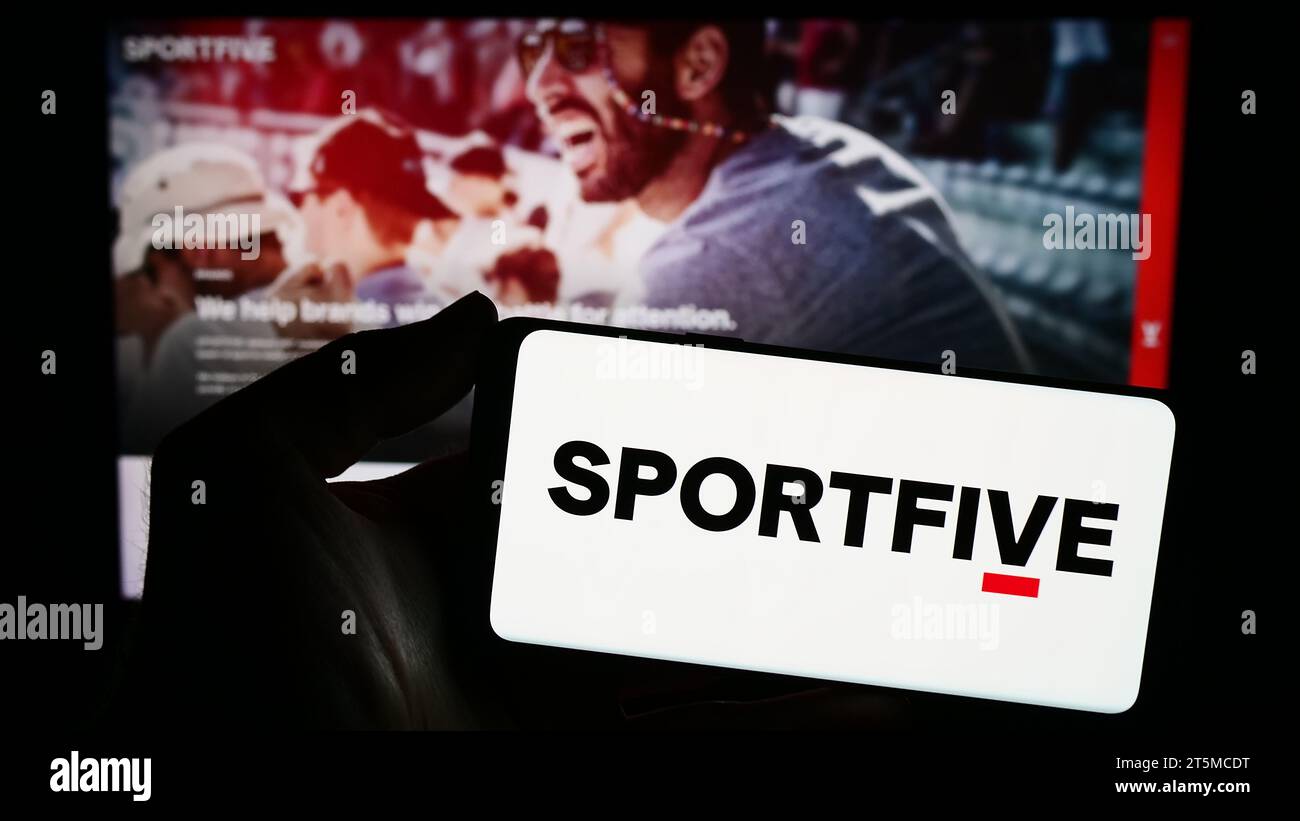 Person mit Smartphone und Logo des internationalen Sportmarketing-Unternehmens Sportfive vor der Website. Schwerpunkt auf dem Display des Telefons. Stockfoto