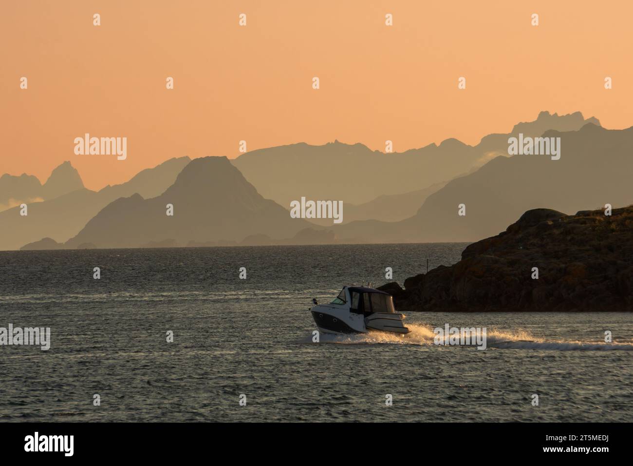 Ein Motorboot in Lofoten, Norwegen, auf dem Meer bei Sonnenuntergang, Berge in der Ferne. Stockfoto