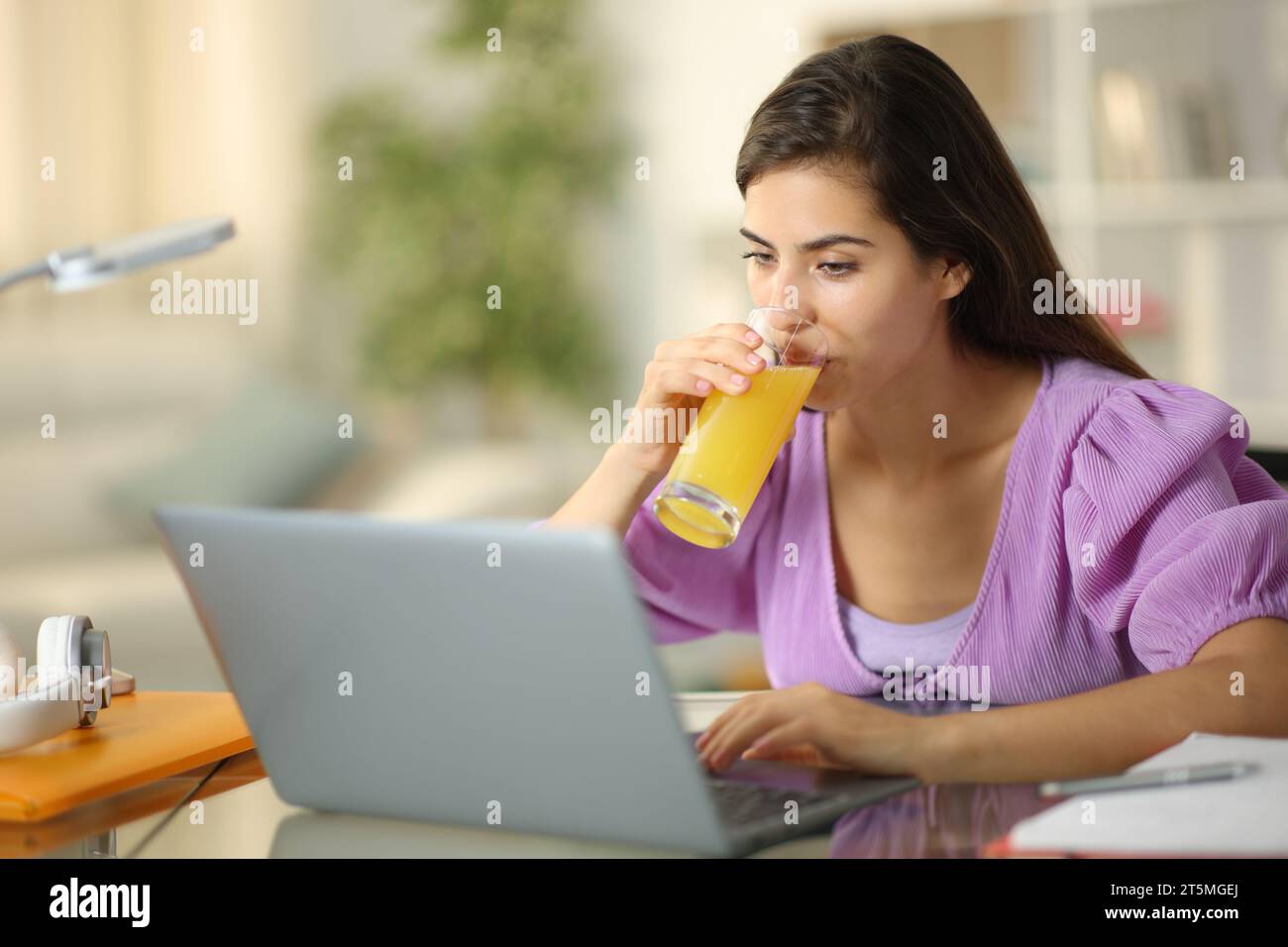 E-Learning-Kurse für Schüler mit Laptop, der zu Hause Orangensaft trinkt Stockfoto