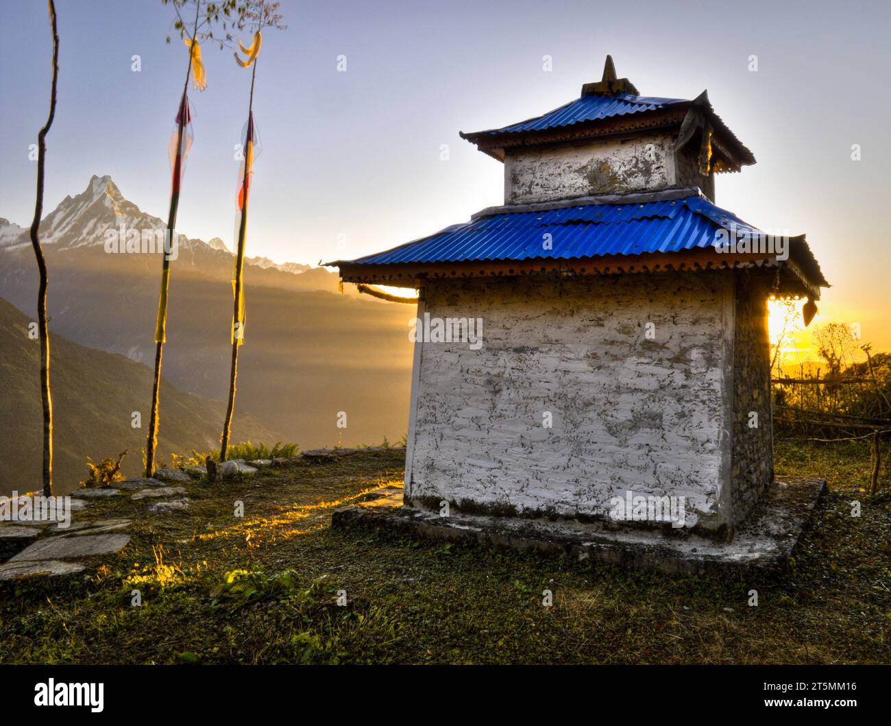 Ein kleines religiöses Schrein-Gebäude befindet sich auf einer grasbewachsenen Terrasse vor einem Berg in der Annapurna-Region in Nepal. Stockfoto