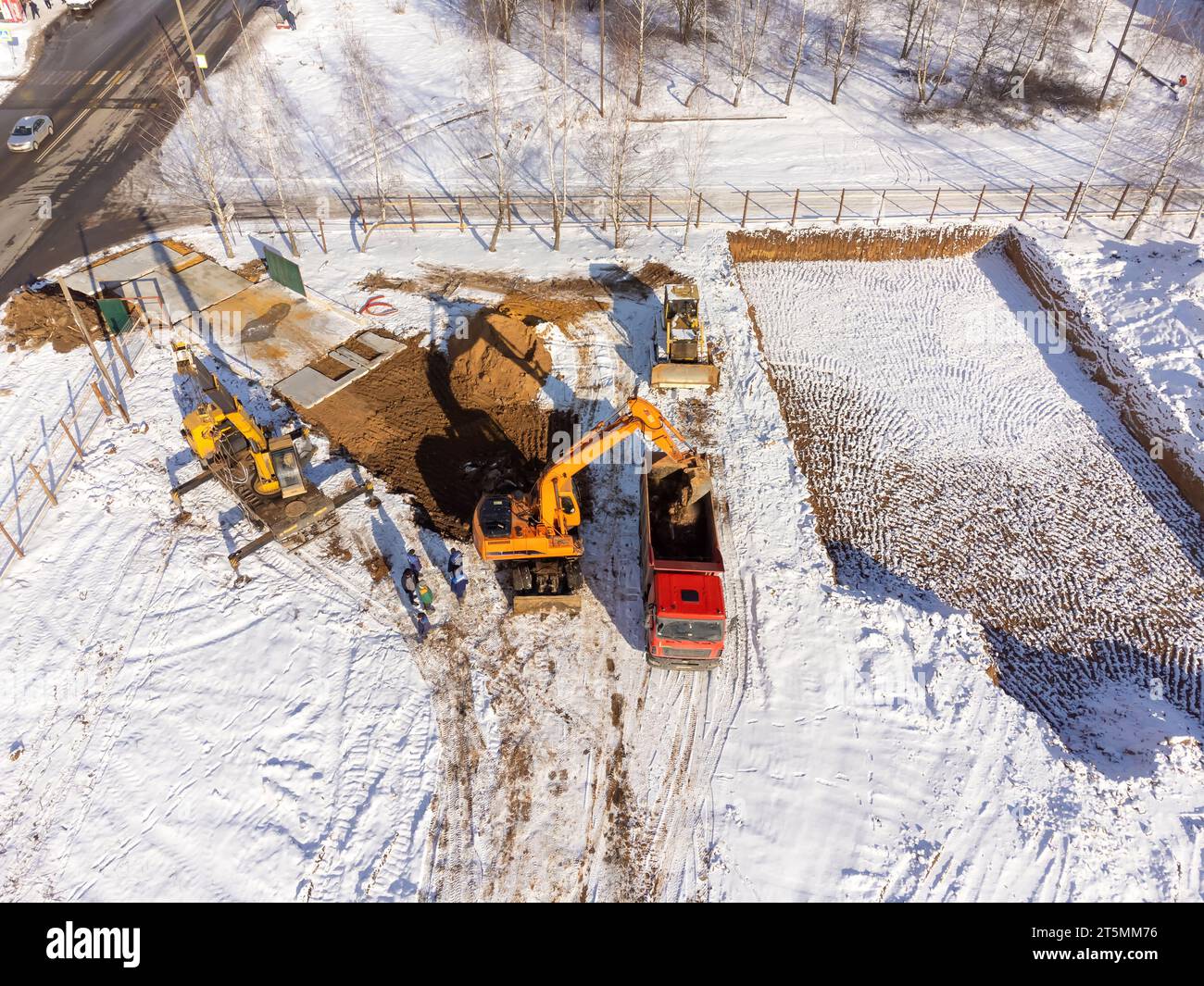 Luftaufnahme eines Baggers, der Sand in einen Lkw gießt. Blick von oben auf die Baustelle im Winter. Schießen von einer Drohne aus. Stockfoto