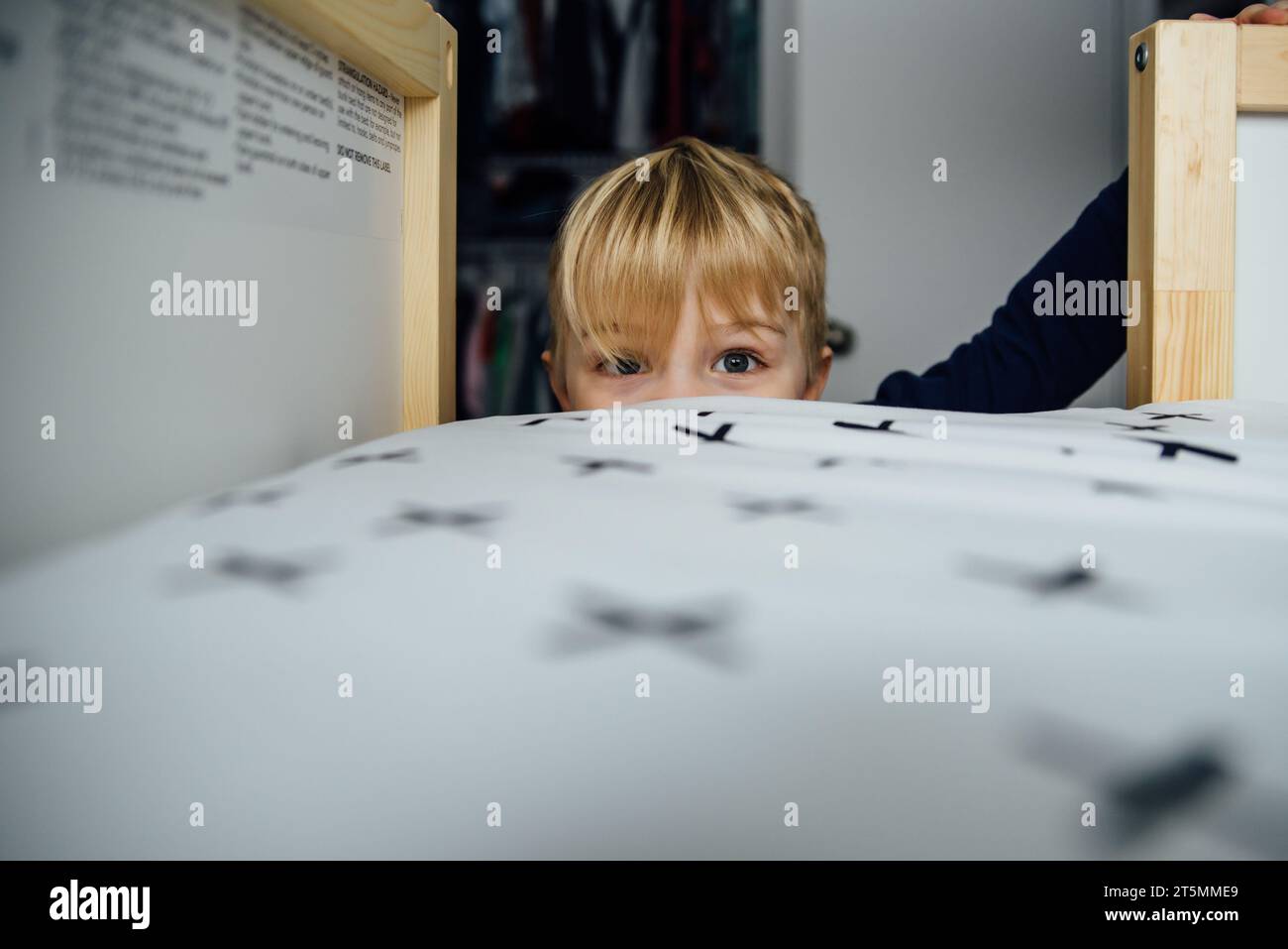 Der Junge guckt über das Bett mit weiten Augen zu Hause vor die Kamera. Stockfoto