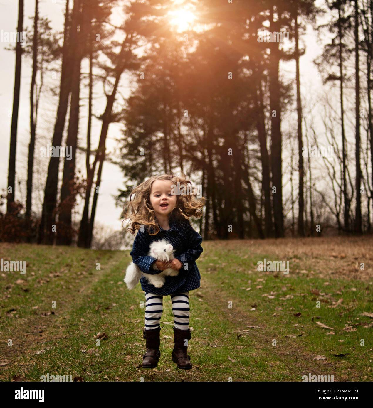 Ein glückliches kleines Mädchen, das mit einem Plüschtier auf dem Feld springt Stockfoto