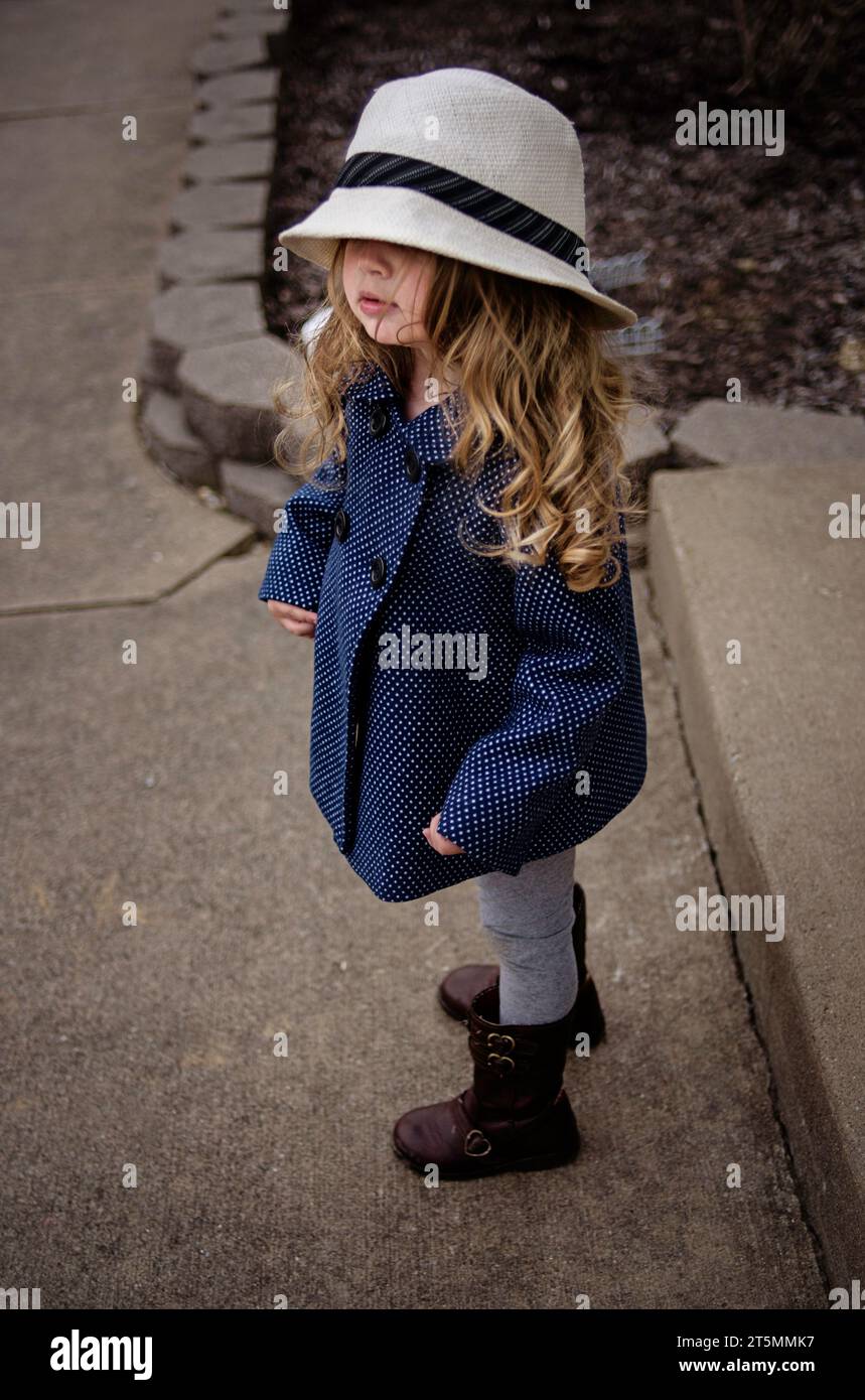 Wunderschönes Kleinkind mit Hut und Erbsenmantel mit langen blonden Locken Stockfoto