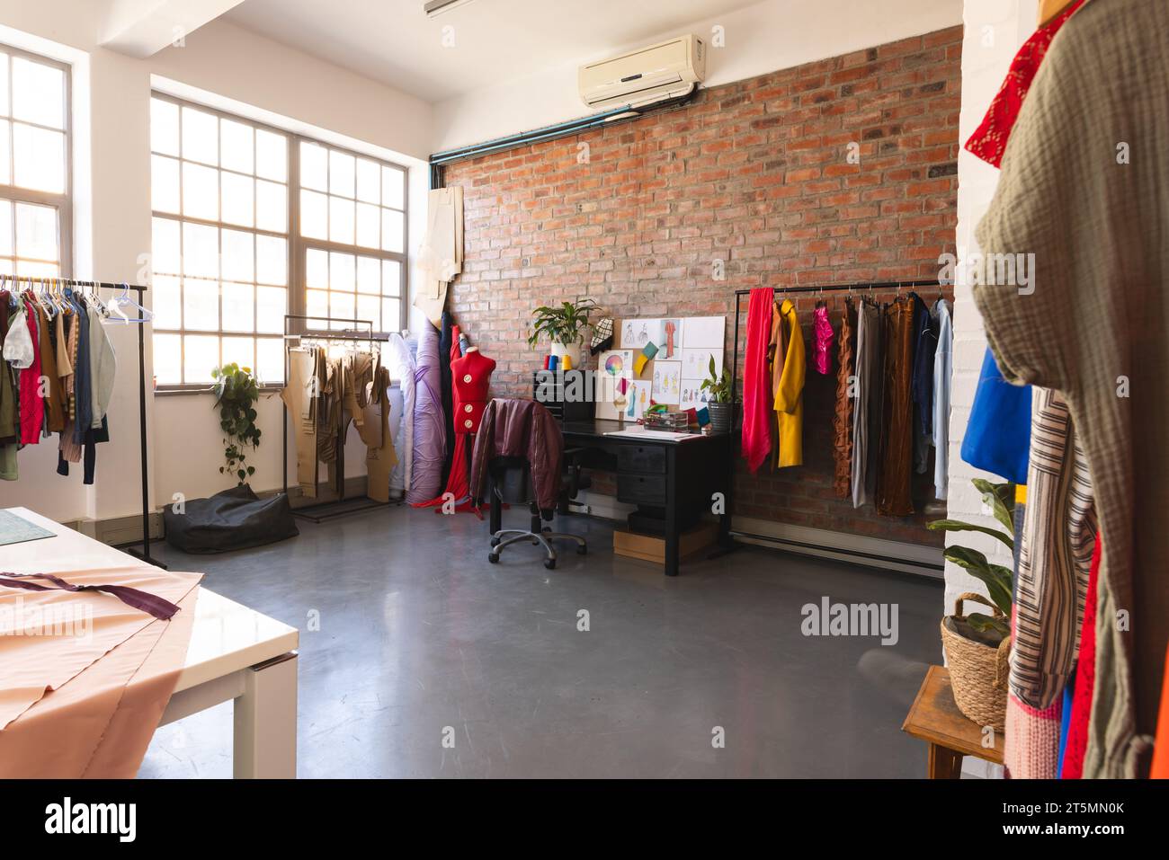 Design auf dem Schreibtisch, farbenfrohe Kleidung und Stoffe im sonnigen Studio Stockfoto