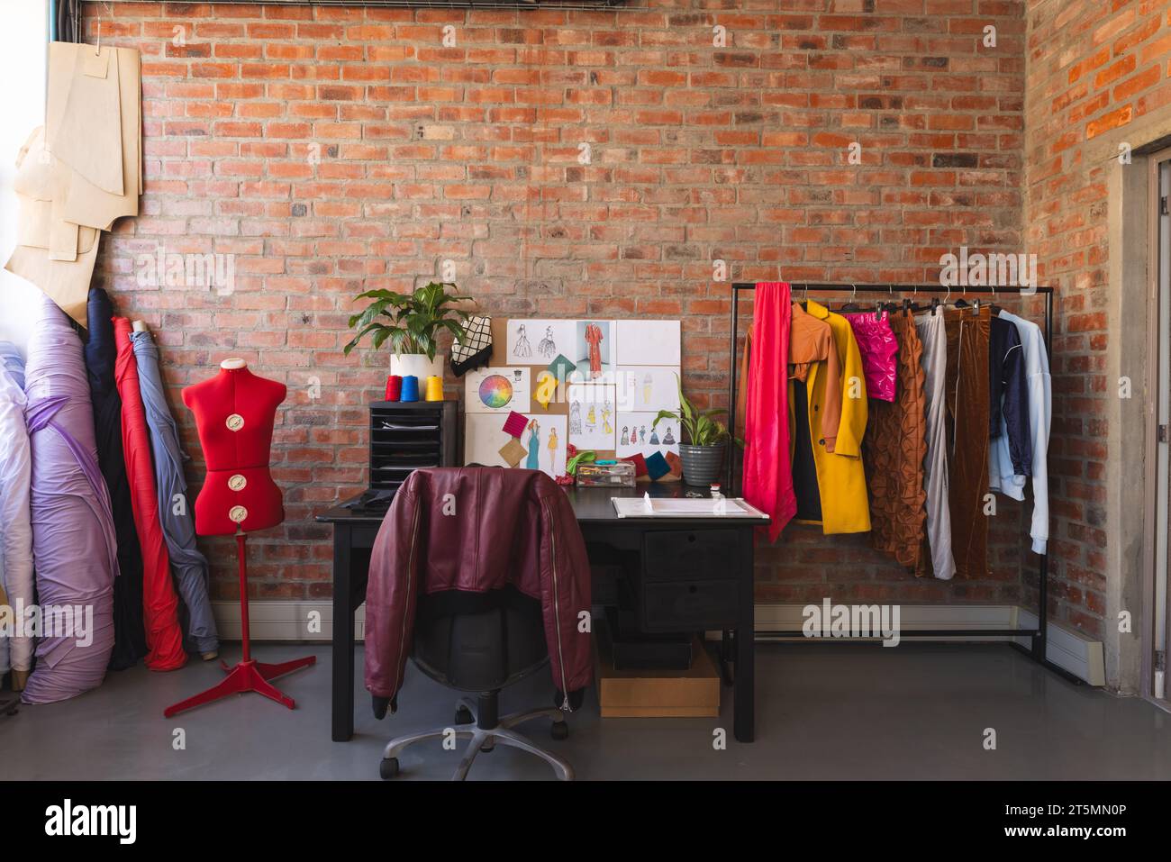 Design auf dem Schreibtisch, farbenfrohe Kleidung und Stoffe im sonnigen Studio Stockfoto