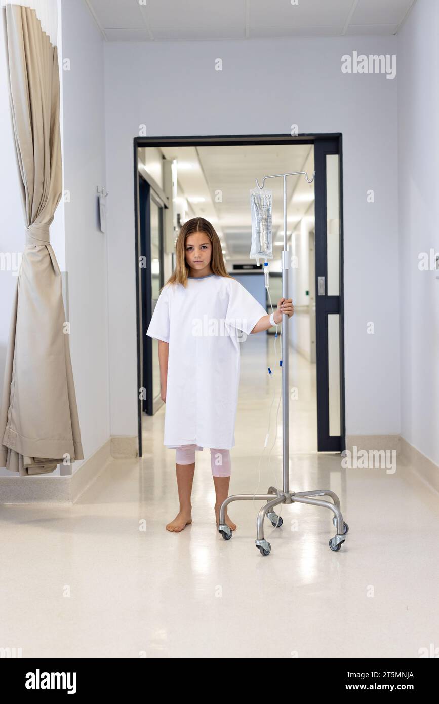 Porträt einer kaukasischen Patientin im Kleid, die mit Tropfständer im Krankenhausflur läuft, Kopierraum Stockfoto