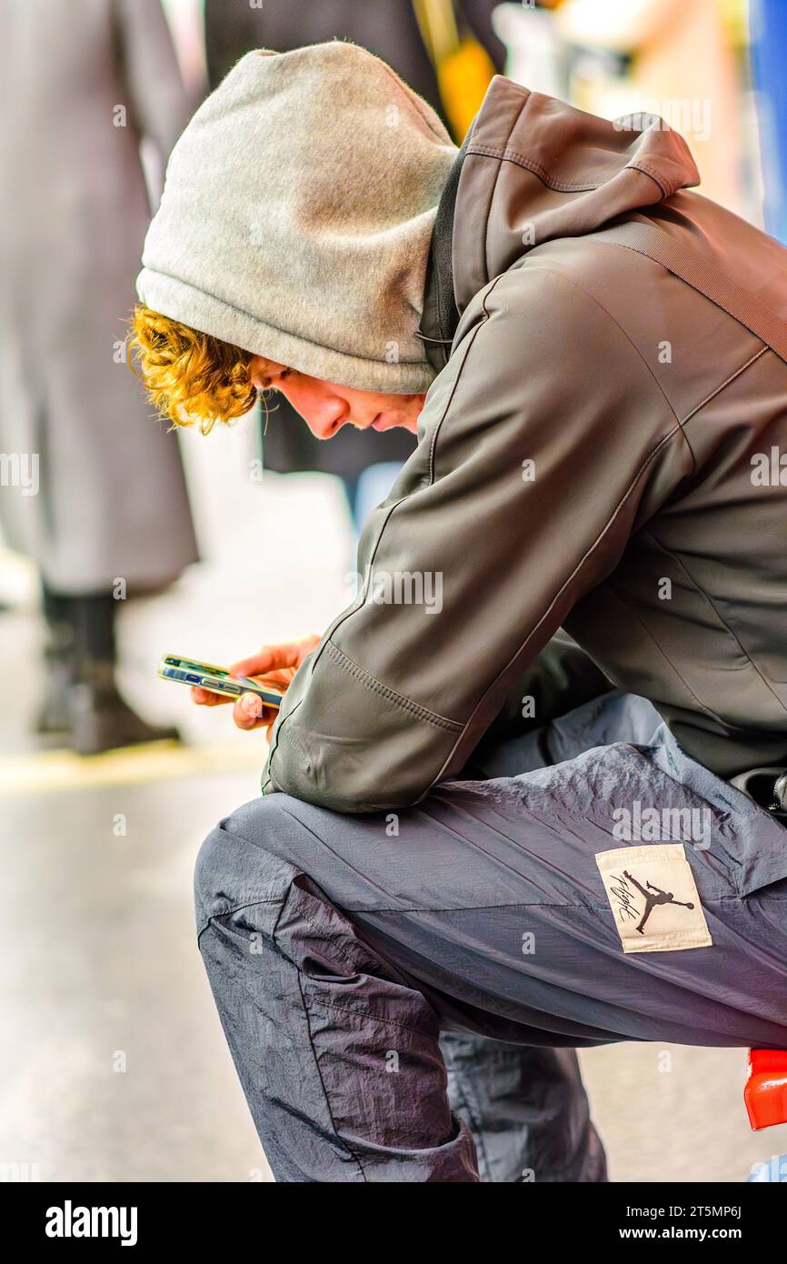 Passagier, der auf das Smartphone blickt, während er auf den Metrozug wartet – Paris, Frankreich. Stockfoto