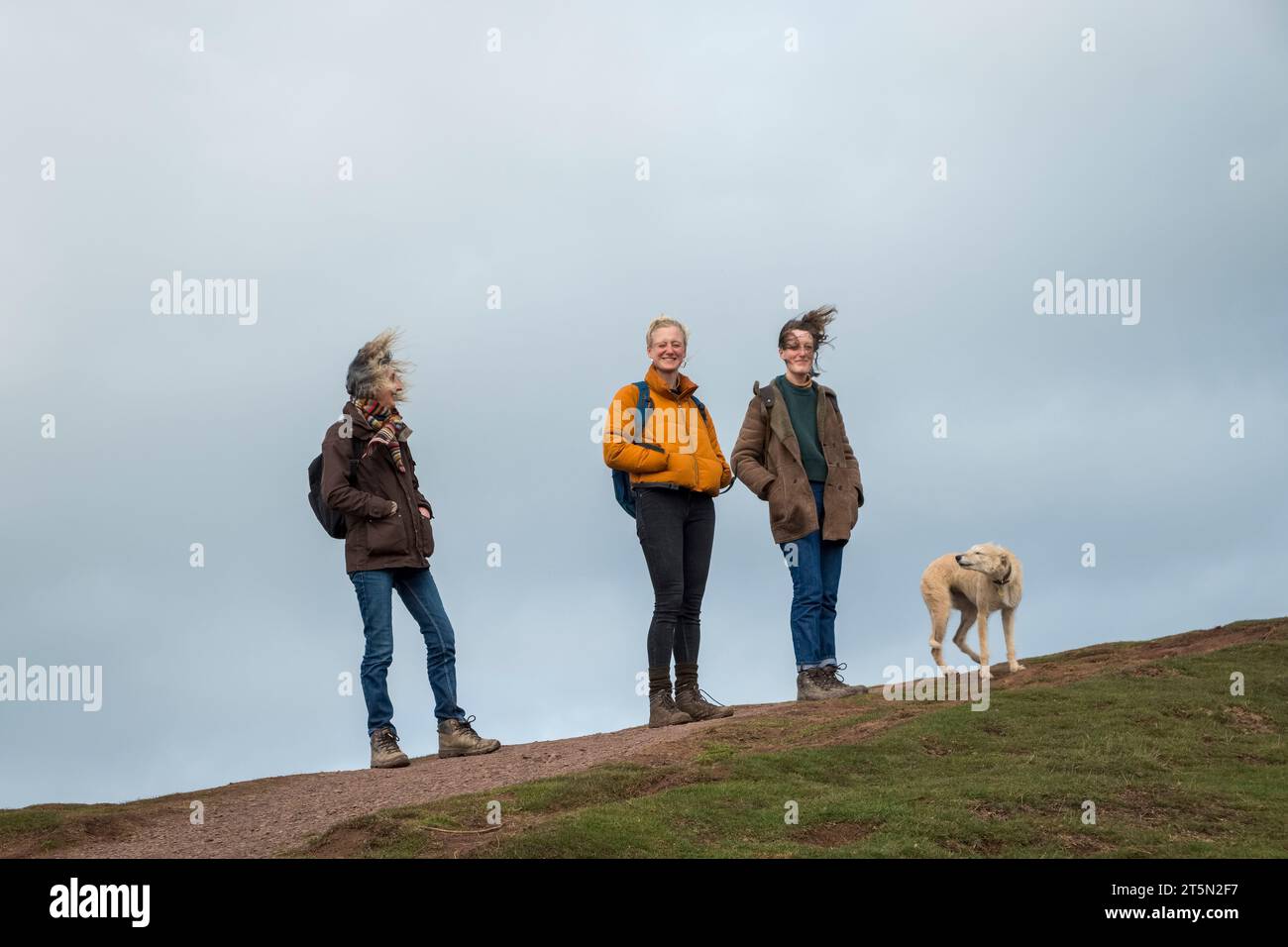 Drei Frauen und ein Hund bei starkem Wind auf dem Skirrid, einem markanten Hügel in der Nähe von Abergavenny, Wales, im Brecon Beacons National Park Stockfoto