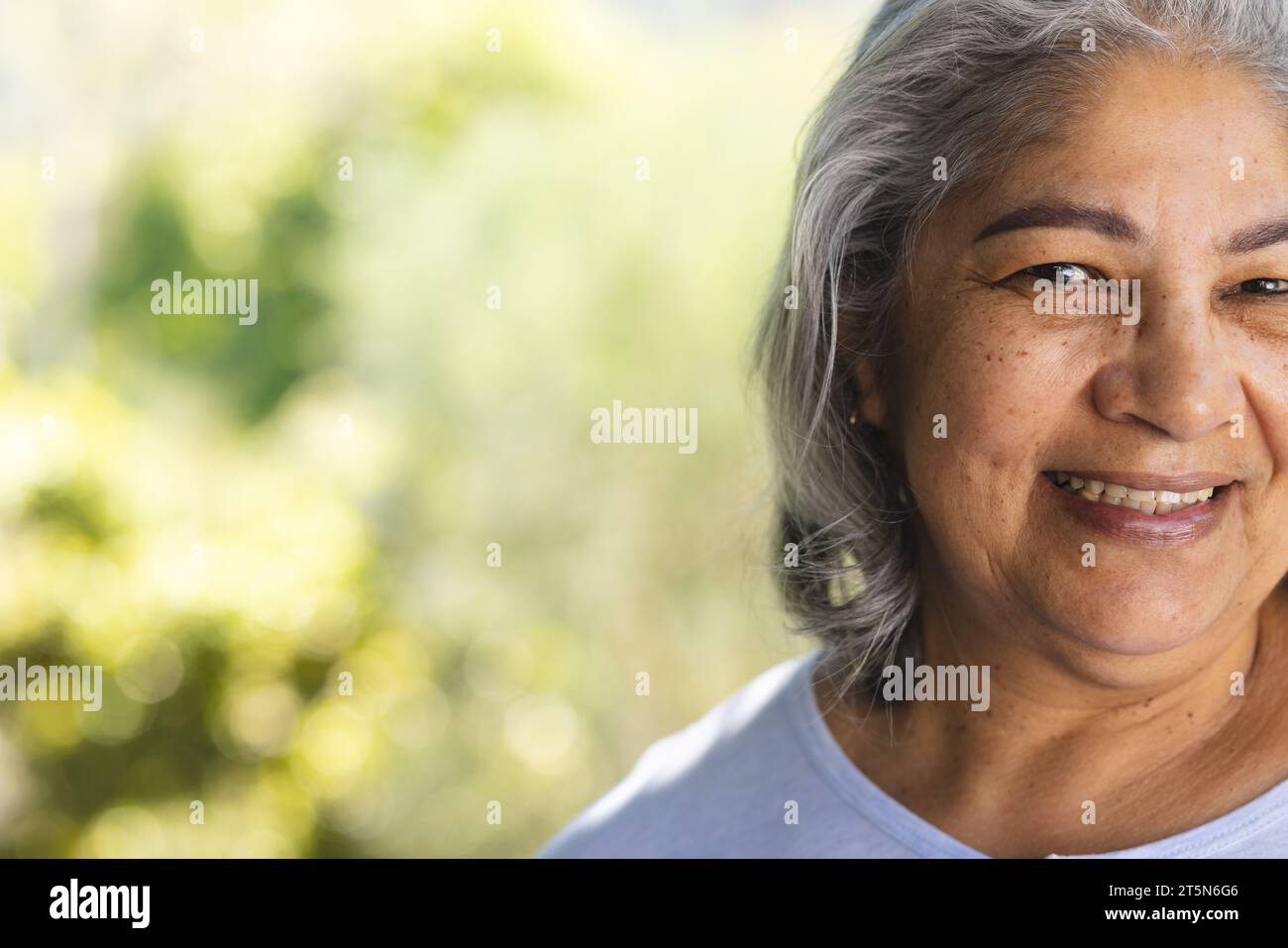 Halbgesicht einer glücklichen, birassischen Seniorin, die im sonnigen Garten lächelt, Kopierraum Stockfoto