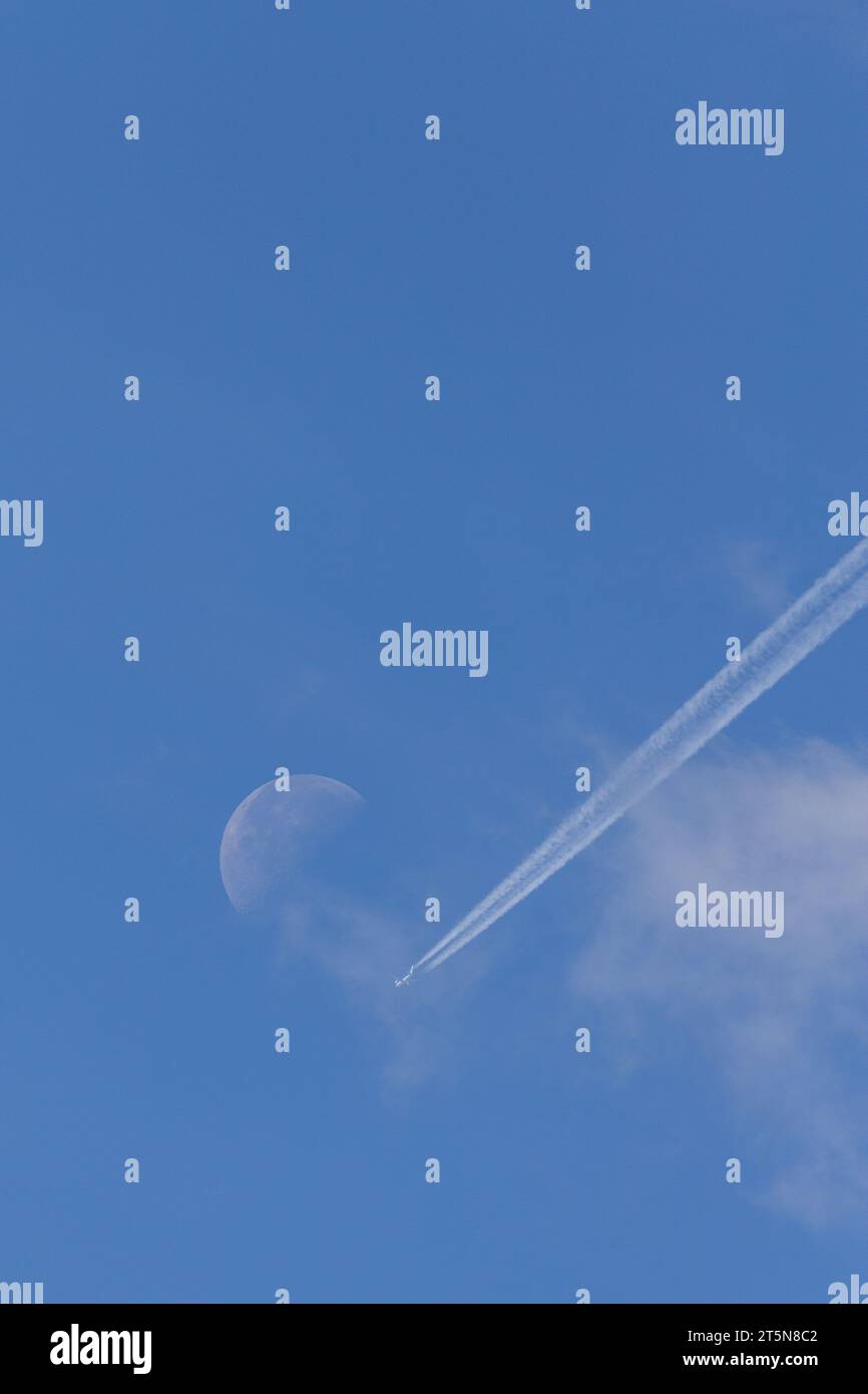 Ein perfekter sonniger Sommertag mit einem Flugzeug und Kondensationspfaden, der in Richtung eines sichtbaren Mondes in der Ferne geht Stockfoto Ein perfekter sonniger Sommertag mit einem Flugzeug und Kondensationspfaden, der in Richtung eines sichtbaren Mondes in der Ferne geht Stockfoto