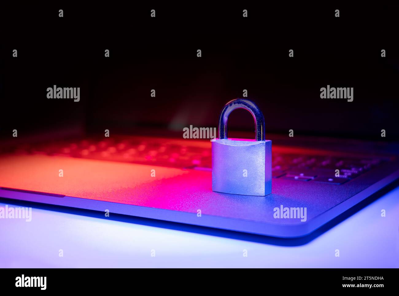 Großaufnahme eines Vorhängeschlosses auf einem Laptop, der mit blauem und rotem Licht beleuchtet ist. Phishing, Cybersicherheitsgefahr oder Ransomware-Angriff. Verschlüsselter Datenschutz in E-Mails. Stockfoto