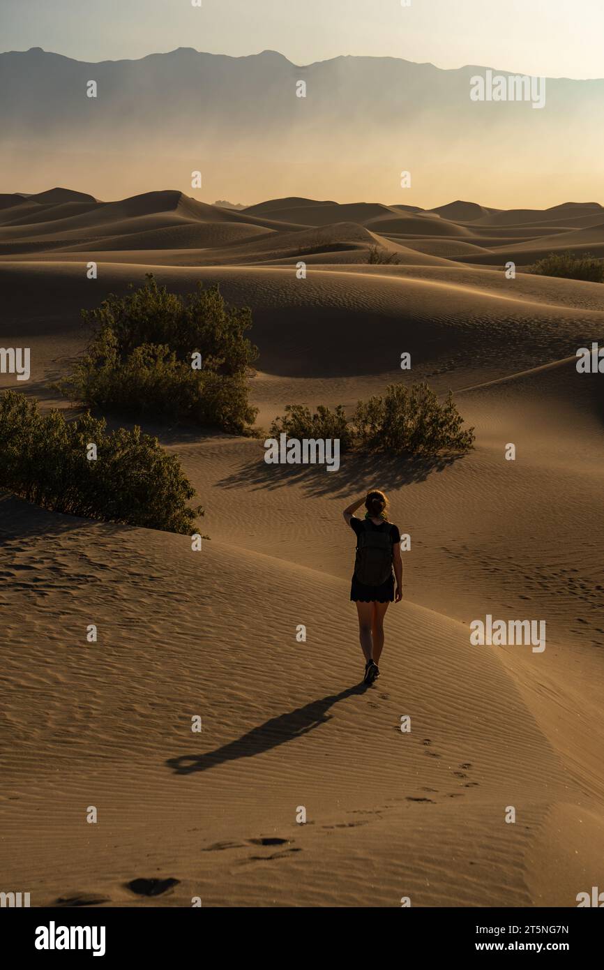 Eine einsame Person, die bei Sonnenaufgang in der Wüste des Death Valley in der Nähe von Mesquite Flats, Kalifornien, spaziert. Helles Licht und trüber Himmel. Stockfoto