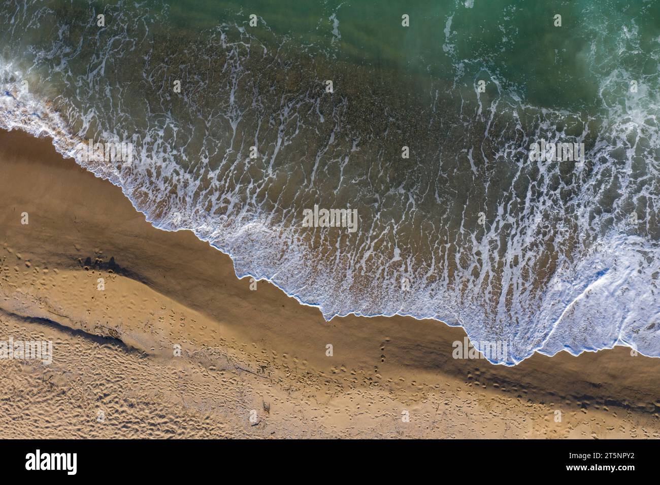 Blick aus der Vogelperspektive auf die Meereswellen, die einen abgelegenen Sandstrand waschen Stockfoto