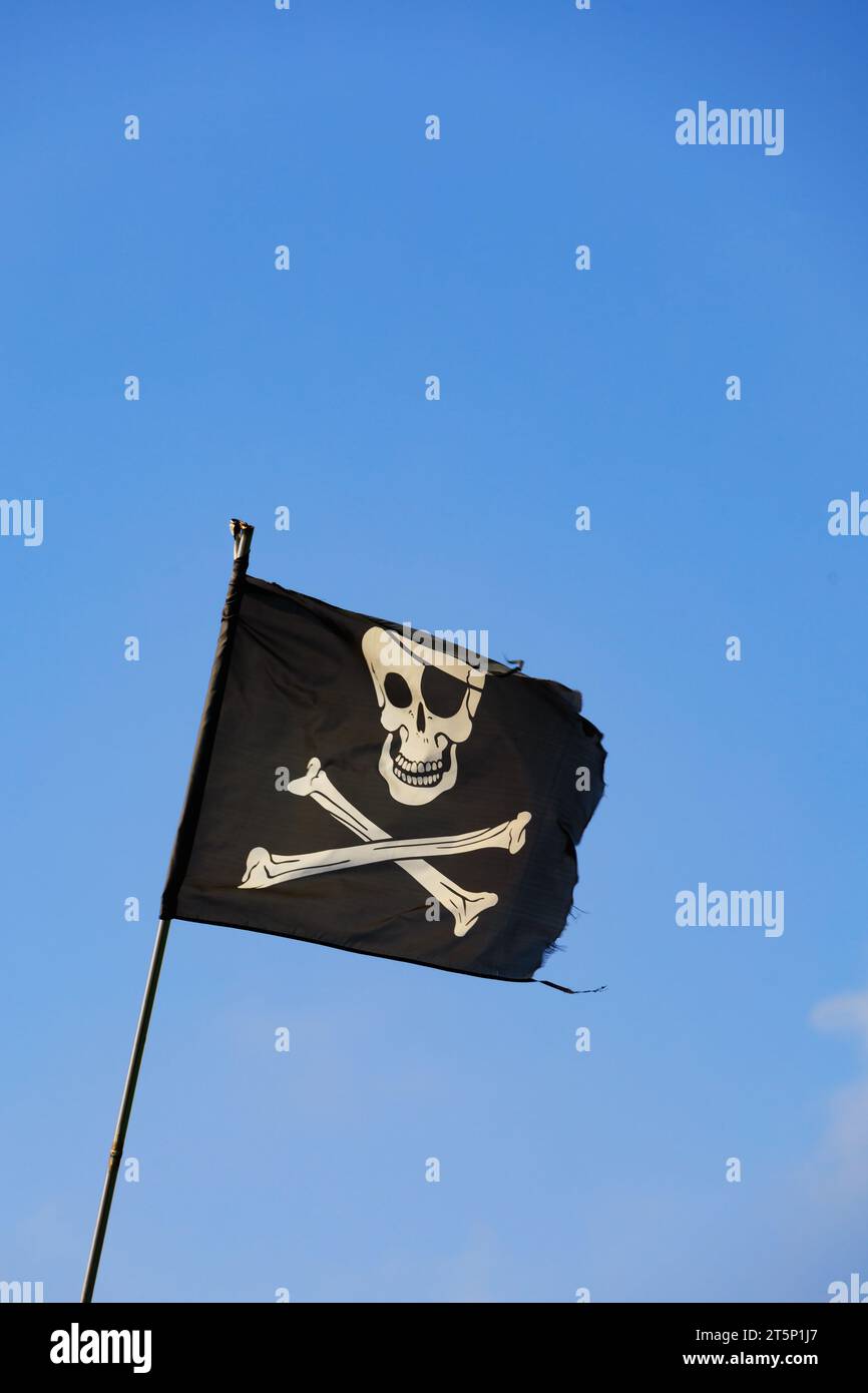 Jolly Roger, Skull und Crossbones schwarze Piratenflagge vor blauem Himmel. Stockfoto