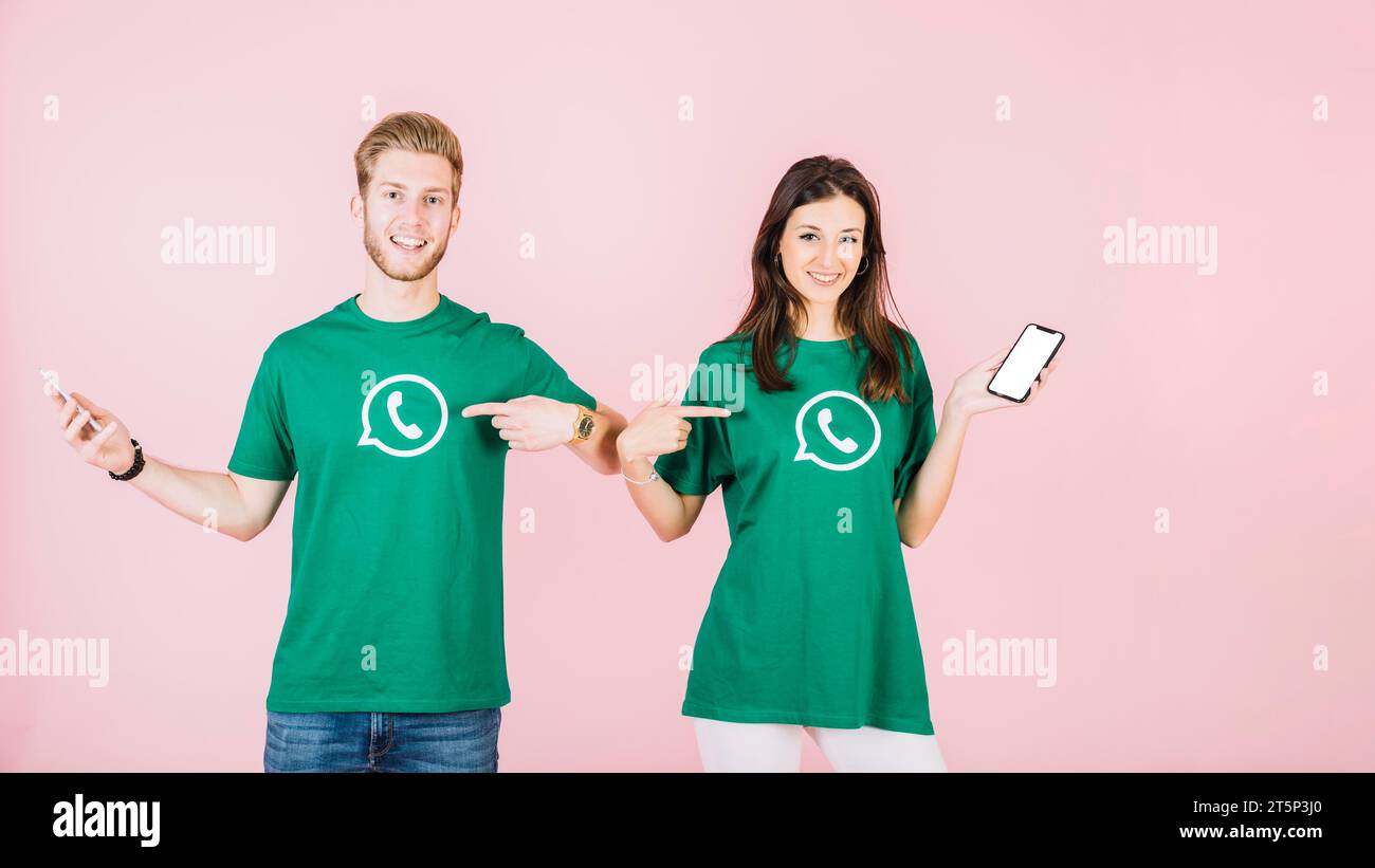 Ein Paar mit einem Handy, das auf sein T-Shirt zeigt, mit dem WhatsApp-Symbol Stockfoto