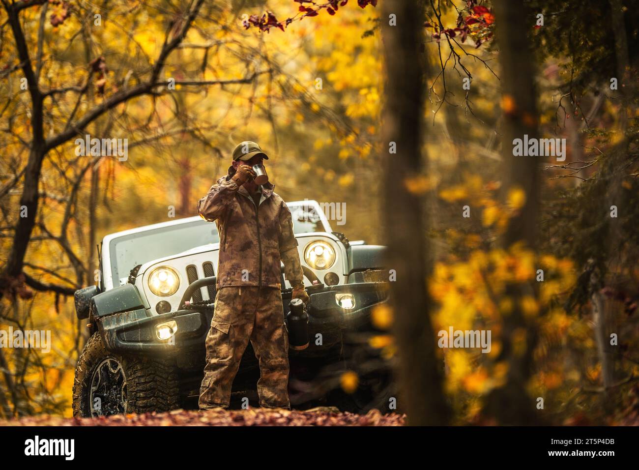 Kaukasischer Hunter trinkt einen Kaffee aus seiner Thermos während des Jagdtages. Fahrzeug mit Allradantrieb im Hintergrund Stockfoto