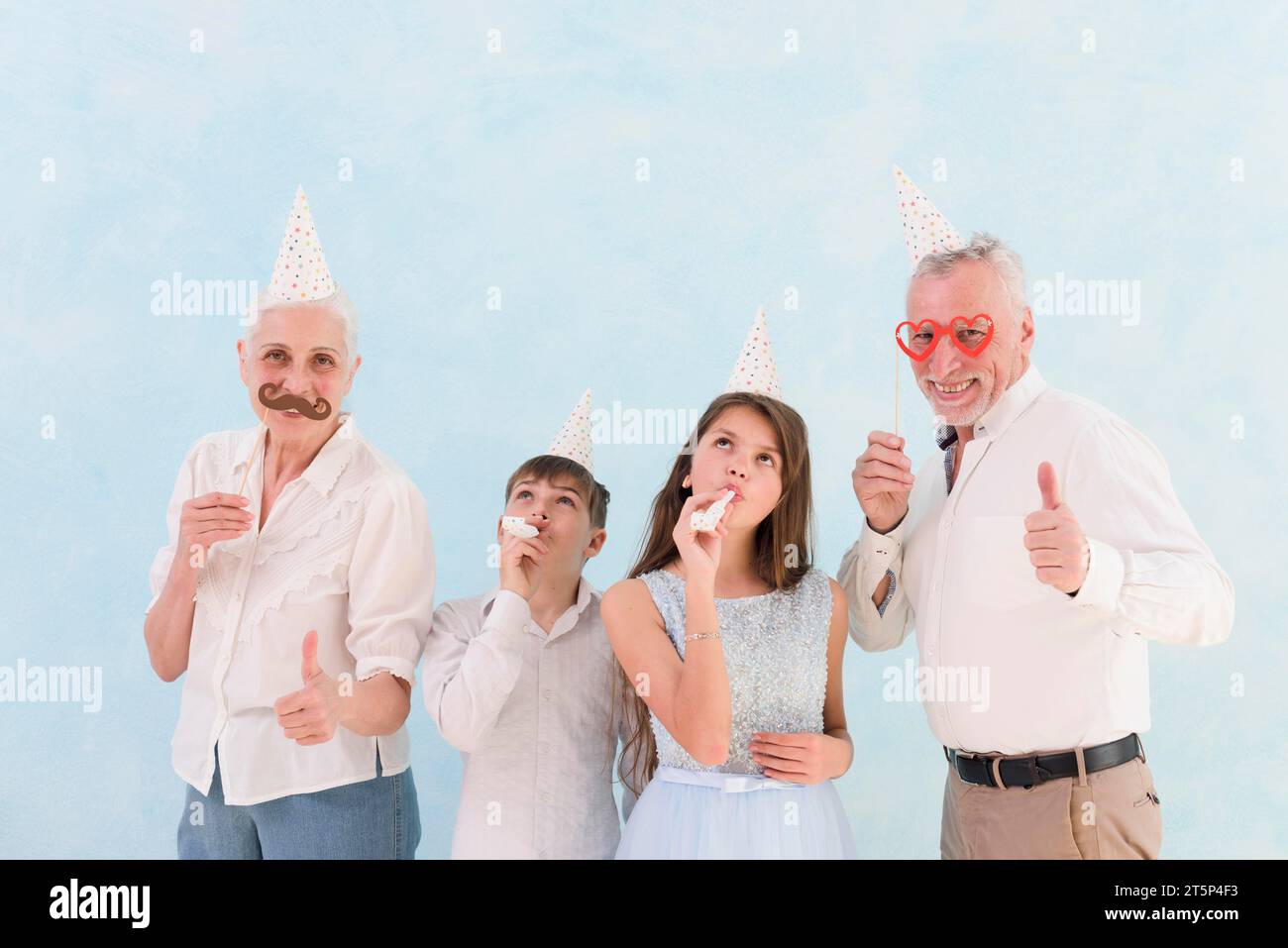 Glückliche Großeltern zeigen Papierrequisiten mit ihren Enkeln, die Partyhörner blasen Stockfoto