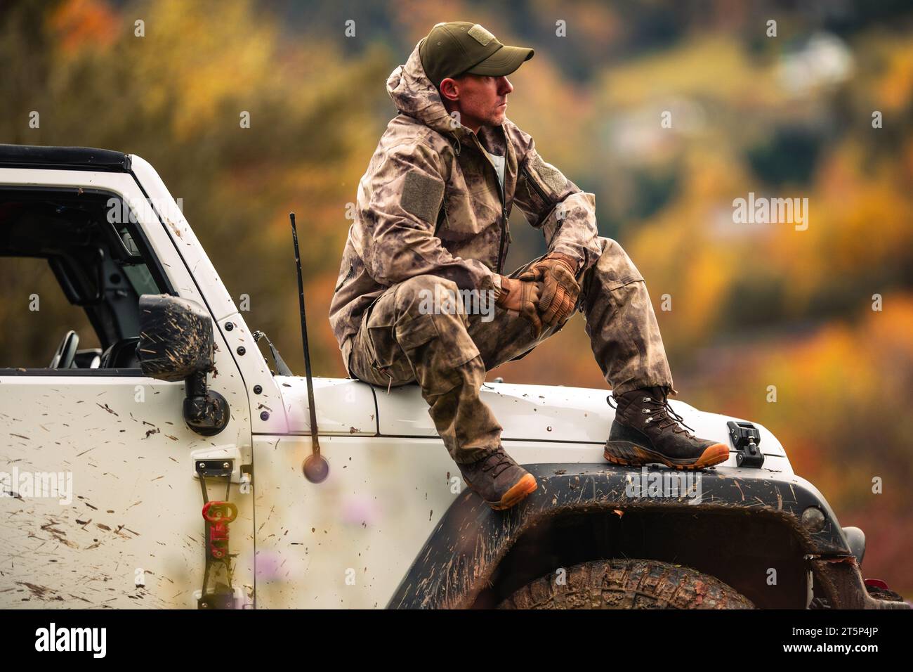 Kaukasischer Hunter in seinen 40er Jahren, der während des Jagdtages auf der Motorhaube seines Allradantriebs sitzt Stockfoto