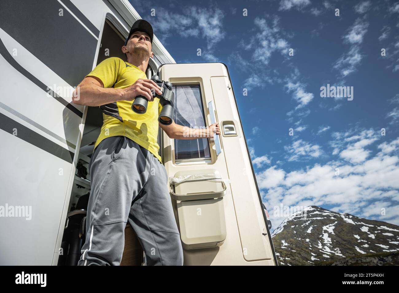 Kaukasischer männlicher Tourist mit Fernglas vor seinem Wohnmobil, der die umliegenden Berge erkundet Stockfoto