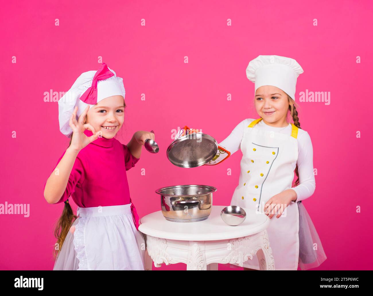 Zwei Mädchen kochen mit Topf und zeigen eine gute Geste Stockfoto