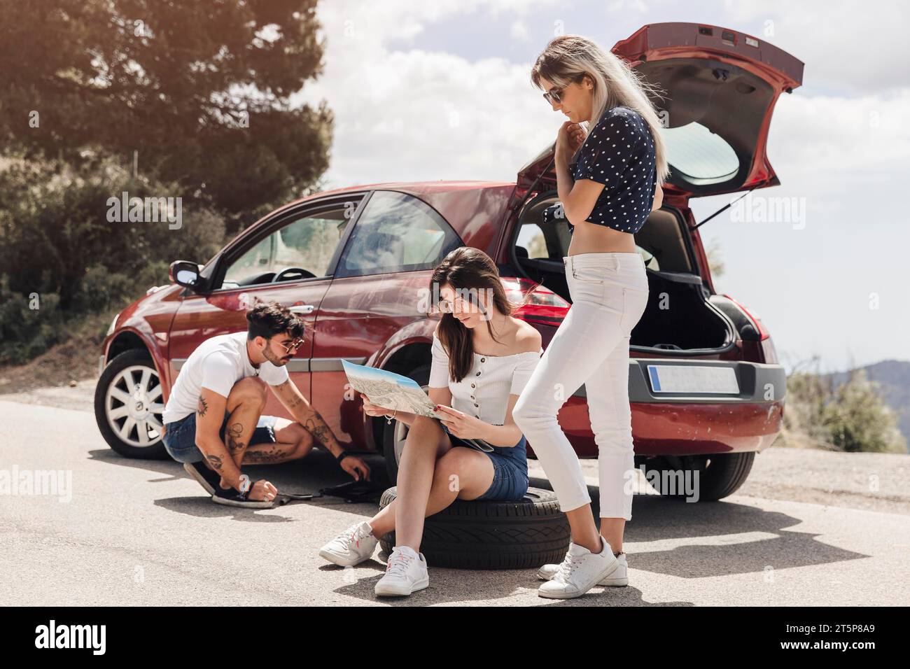 Eine weibliche Karte in der Nähe eines Mannes, der ein kaputtes Auto untersucht Stockfoto