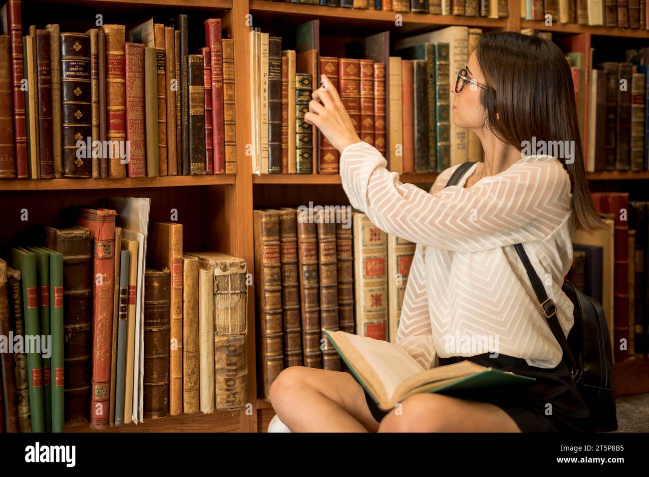 Studentin sitzend im Kreuz mit offener Bücherbibliothek Stockfoto