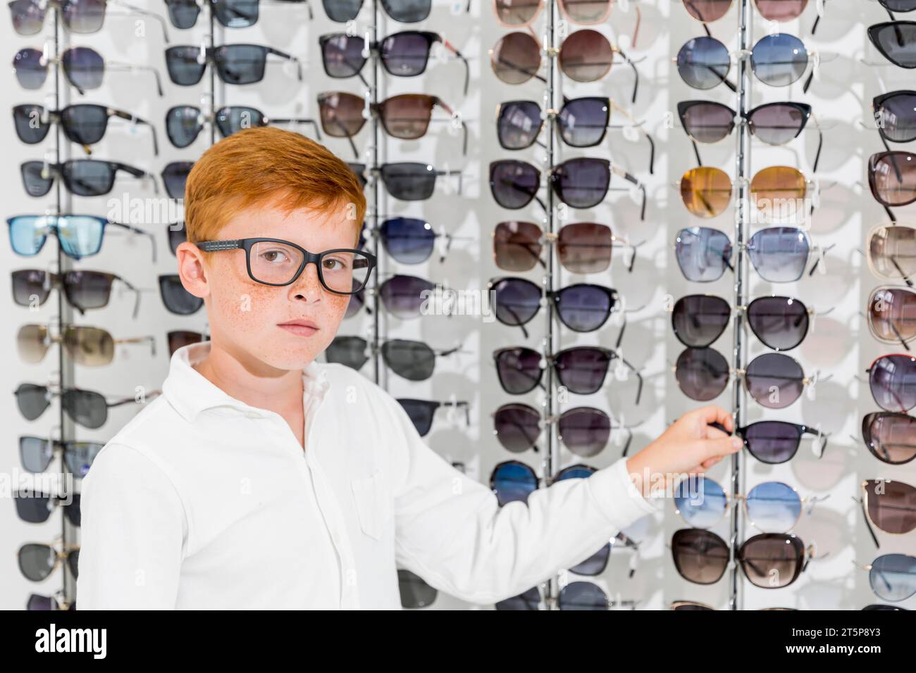 Unschuldiger Junge, der Kamera weiß aussieht, hält Brillenoptik-Geschäft Stockfoto