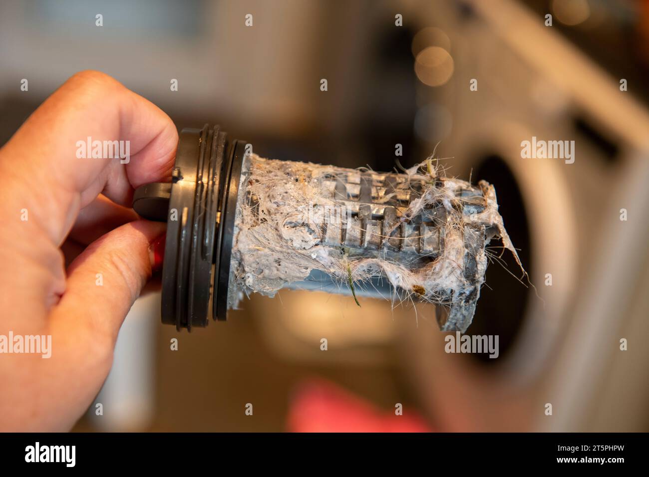 Verstopfter verschmutzter Filter in der Waschmaschine, voller Haare und Kalk, Maschine im Hintergrund Stockfoto