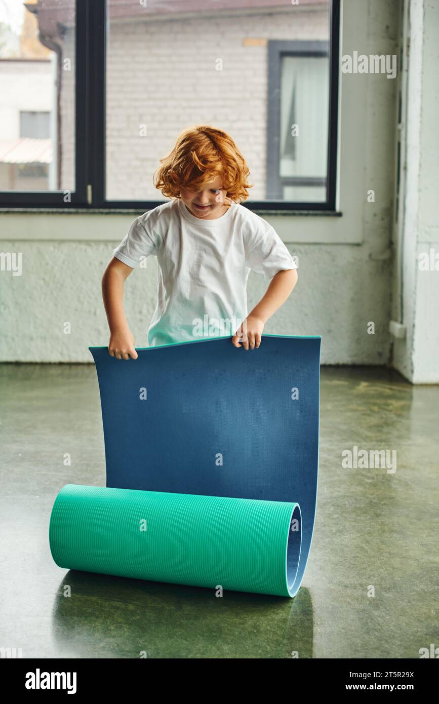 Vertikale Aufnahme eines vorpubertären rothaarigen Jungen im Sportbekleidung-Faltkaremat, Kindersport Stockfoto