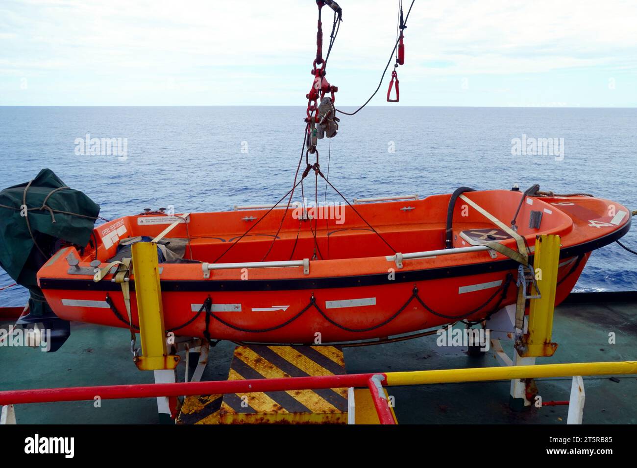 Orangefarbenes Rettungsboot mit Außenbordmotor aus glasfaserverstärktem Kunststoff ist durch einen Davit-Haken gesichert. Stockfoto