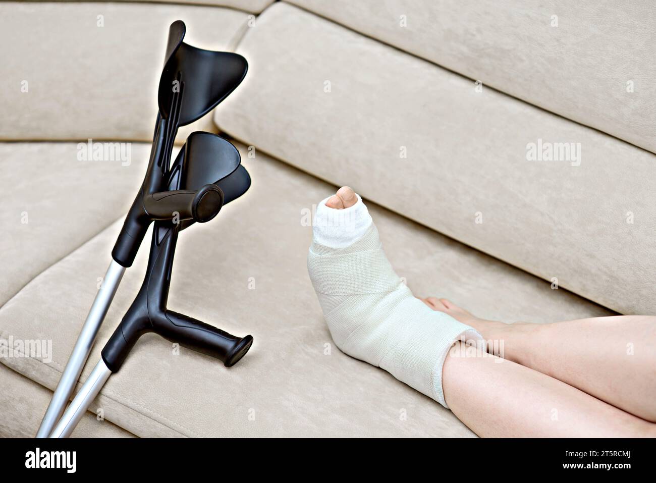 Weibliches gebrochenes Bein in einem Gips neben einer Krücken, die noch Sehnen, Muskeln und Bänder stark hält. Verletzung, Trauma, Genesung, Rehabilitation Stockfoto