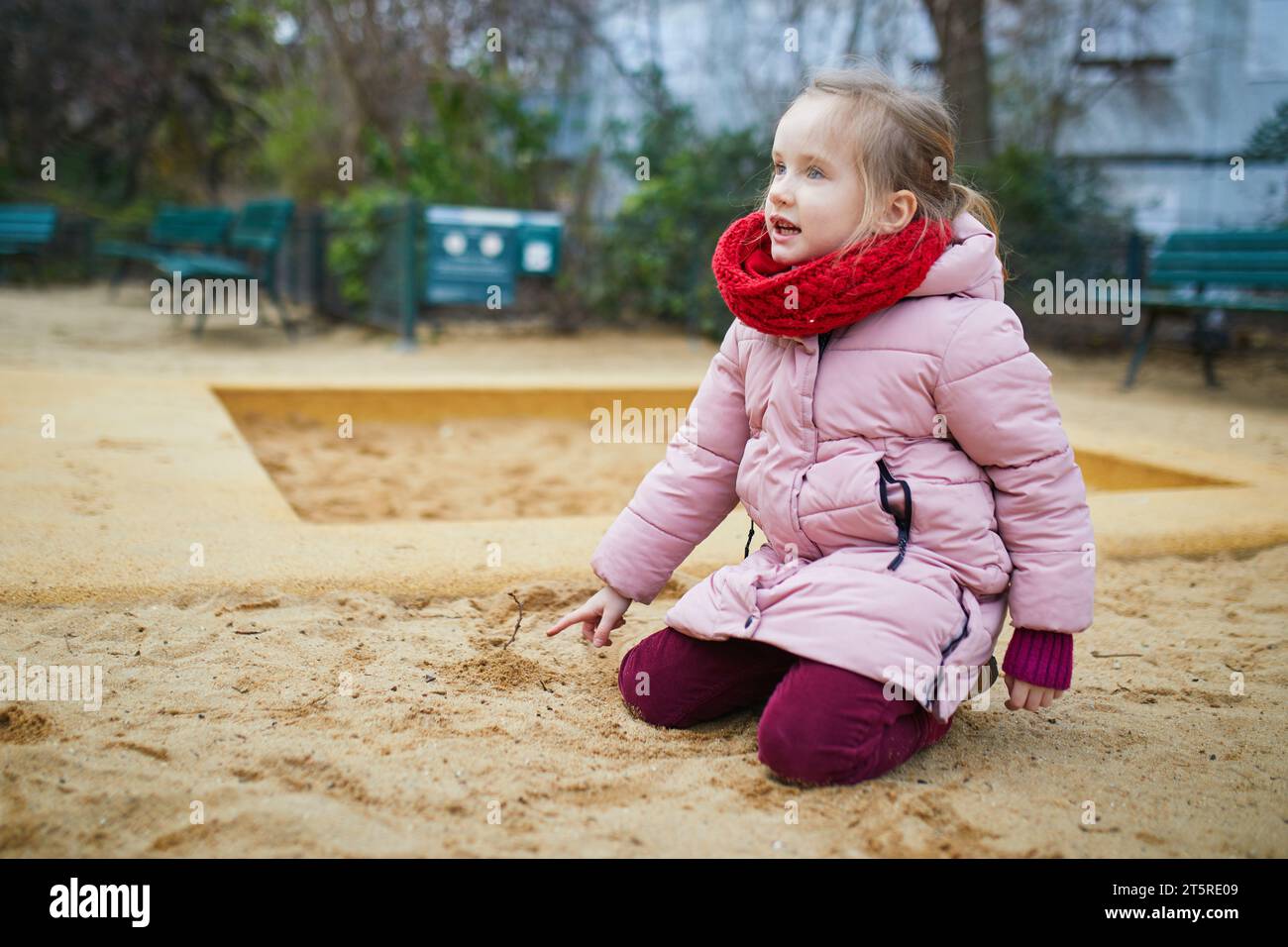 Niedliches Mädchen im Vorschulalter, das am Wintertag Spaß auf dem Spielplatz im Sandkasten hat. Kind, das mit Sandformen spielt und Schlammkuchen macht. Kreative Outdoor-Aktivitäten Stockfoto