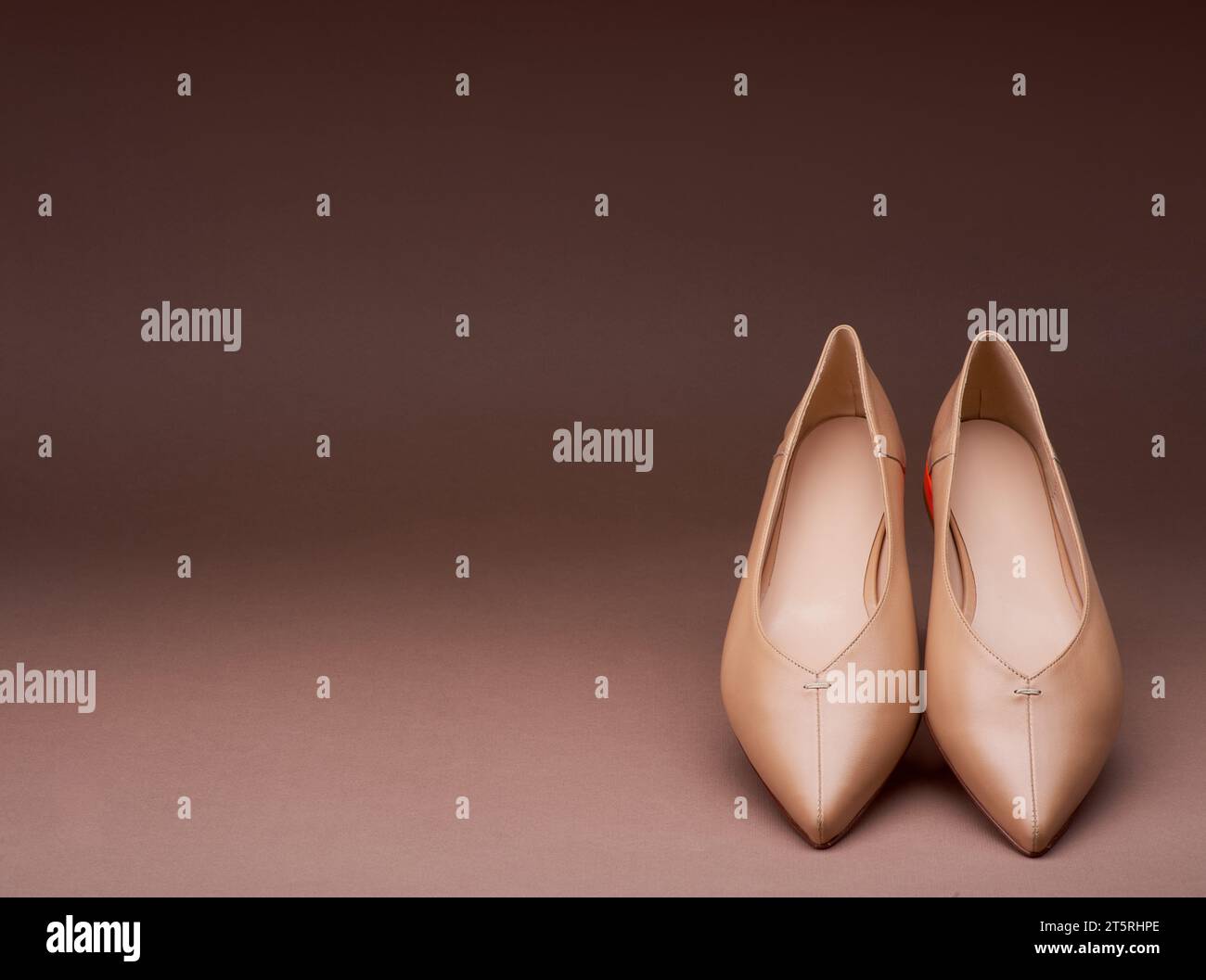 Ein Paar elegante beige, spitz zulaufende Low-Heels-Schuhe in einem Winkel und einer Neigung auf einem abgestuften braunen Hintergrund mit Kopierraum. Minimalistisches Layout mit Stockfoto