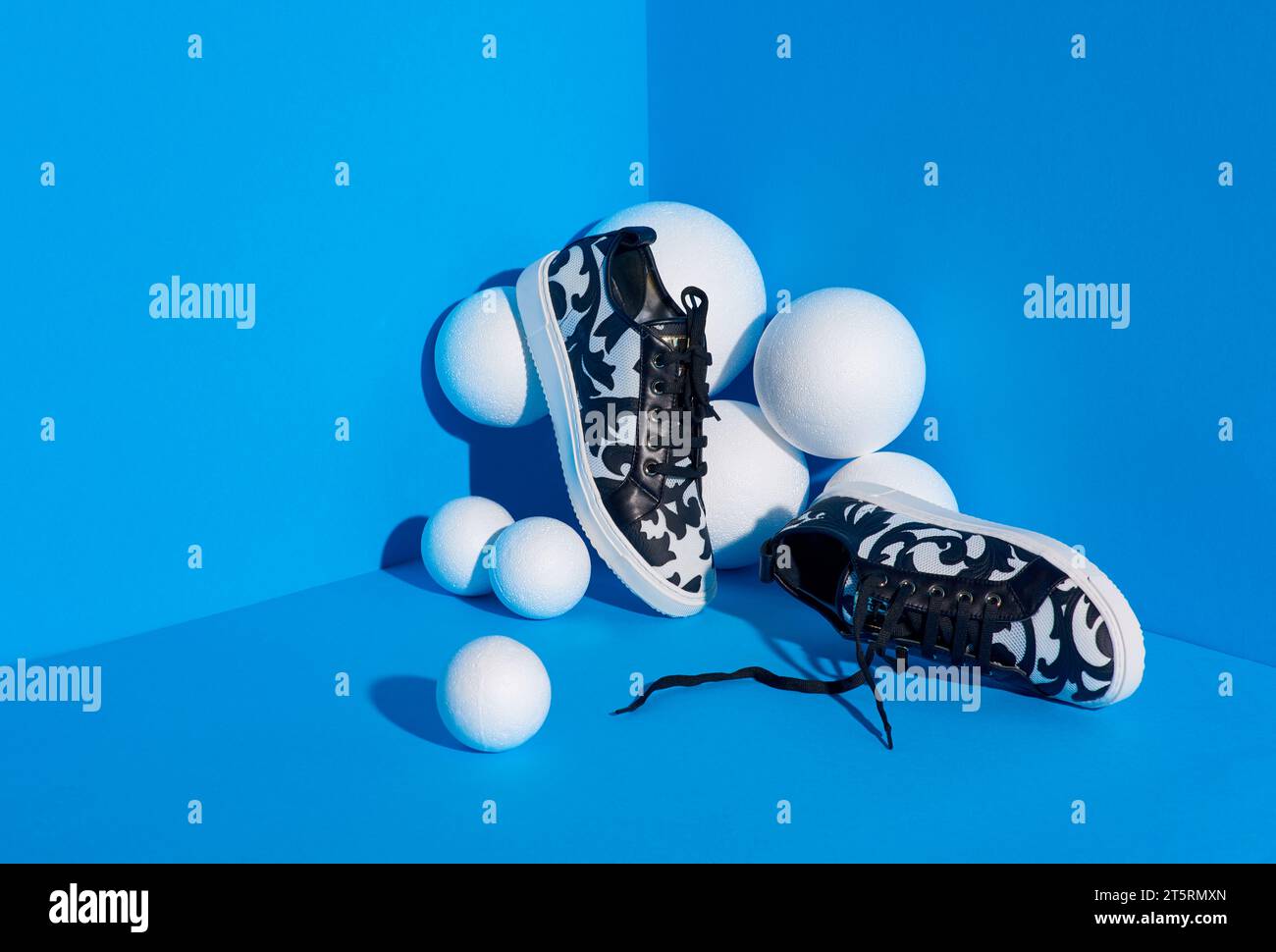 Bequeme weiße und schwarze Damen-Sneaker aus Mesh-Material mit originellem Muster, umgeben von mehreren weißen strukturierten Kugeln im hellen blau Stockfoto