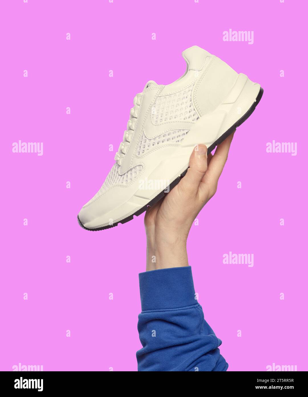 Die Hand des Mannes hält einen modernen weißen Sneaker isoliert auf einem lilafarbenen Hintergrund. Sport und aktiver Lebensstil. Werbekampagne zum Verkauf von Schuhen Stockfoto