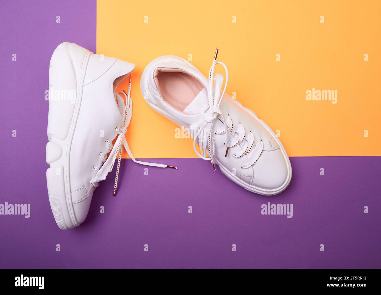 Blick von oben auf moderne weiße Damen-Sneakers mit groben Plateausohlen und glänzenden Schnürsenkeln auf lila-orangefarbenem Hintergrund. Modell für Stockfoto