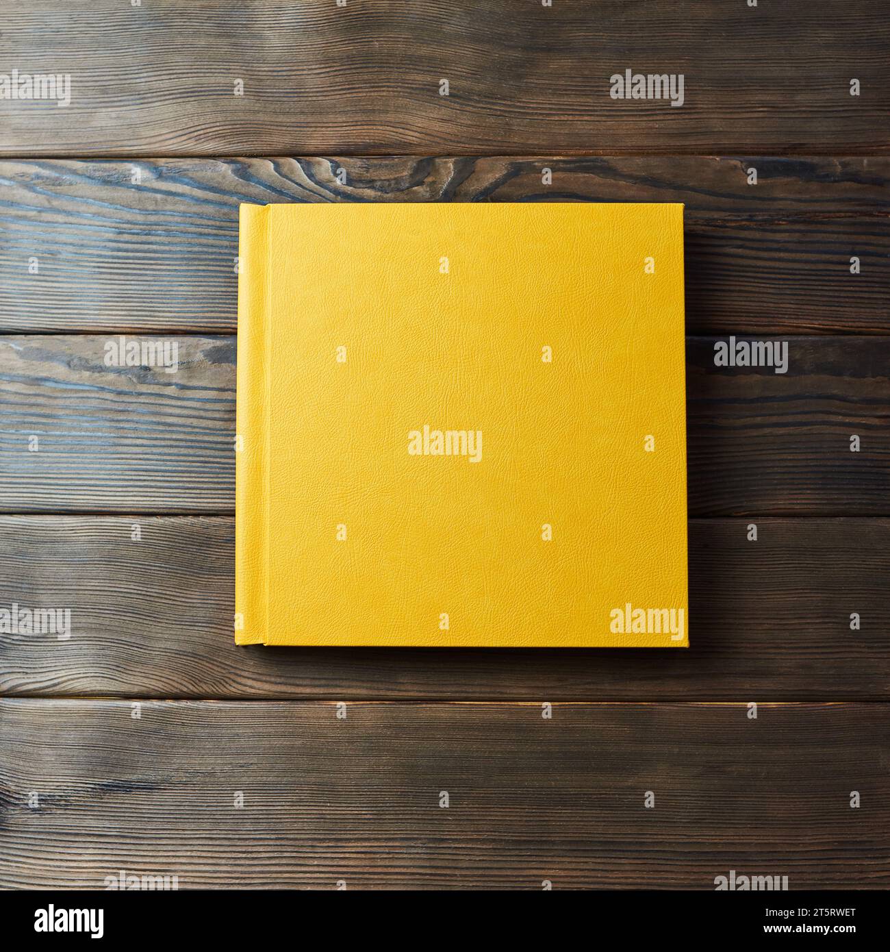 Gelbes Hardcover-Fotobuch isoliert auf einem hölzernen Hintergrund mit Kopierraum. Draufsicht, flach. Leeres Modell für geschlossenes Buch zum Platzieren von benutzerdefiniertem Text oder im Stockfoto