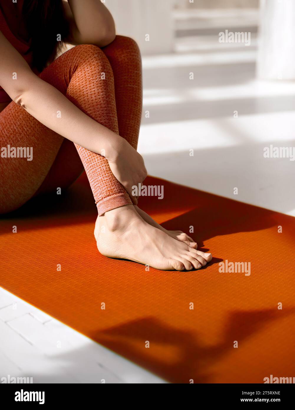 Nahaufnahme von weiblichen Füßen, die sich auf einer orangefarbenen Yogamatte entspannen. Physiotherapie, Reflexologie, Flexibilitätsförderung. Weniger Muskelkater, Inkreas Stockfoto