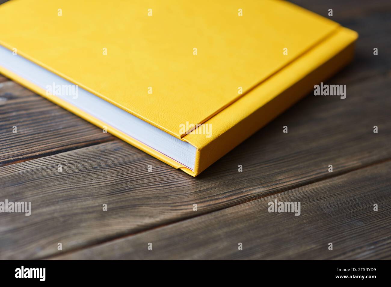 Gelbes Hardcover-Fotobuch isoliert auf einem hölzernen Hintergrund mit Kopierraum. Perspektivische Ansicht. Leeres Modell für geschlossenes Buch zum Platzieren von benutzerdefiniertem Text oder Bild Stockfoto